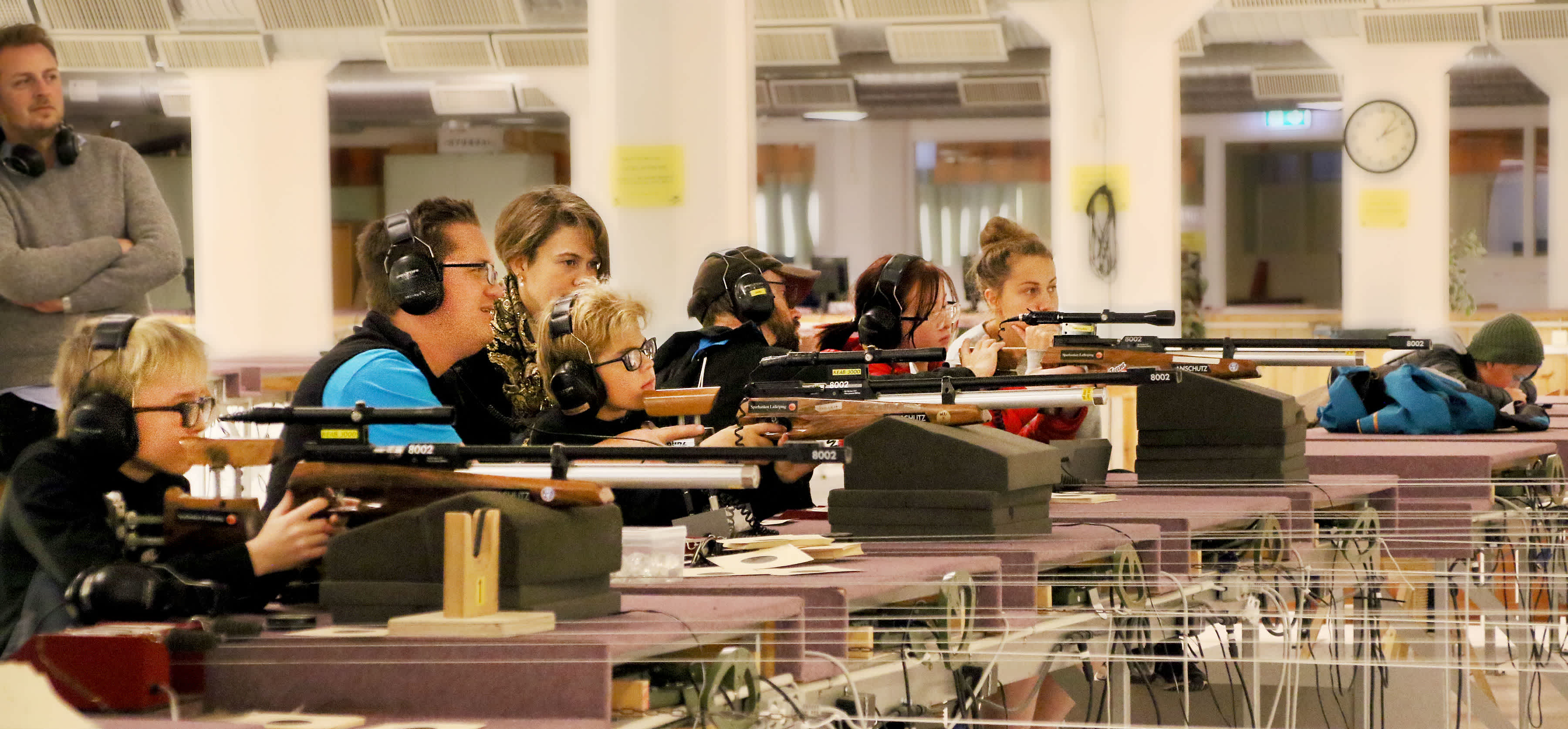 En grupp människor sitter på rad och siktar med elektroniska gevär. De har hörselkåpor över öronen.