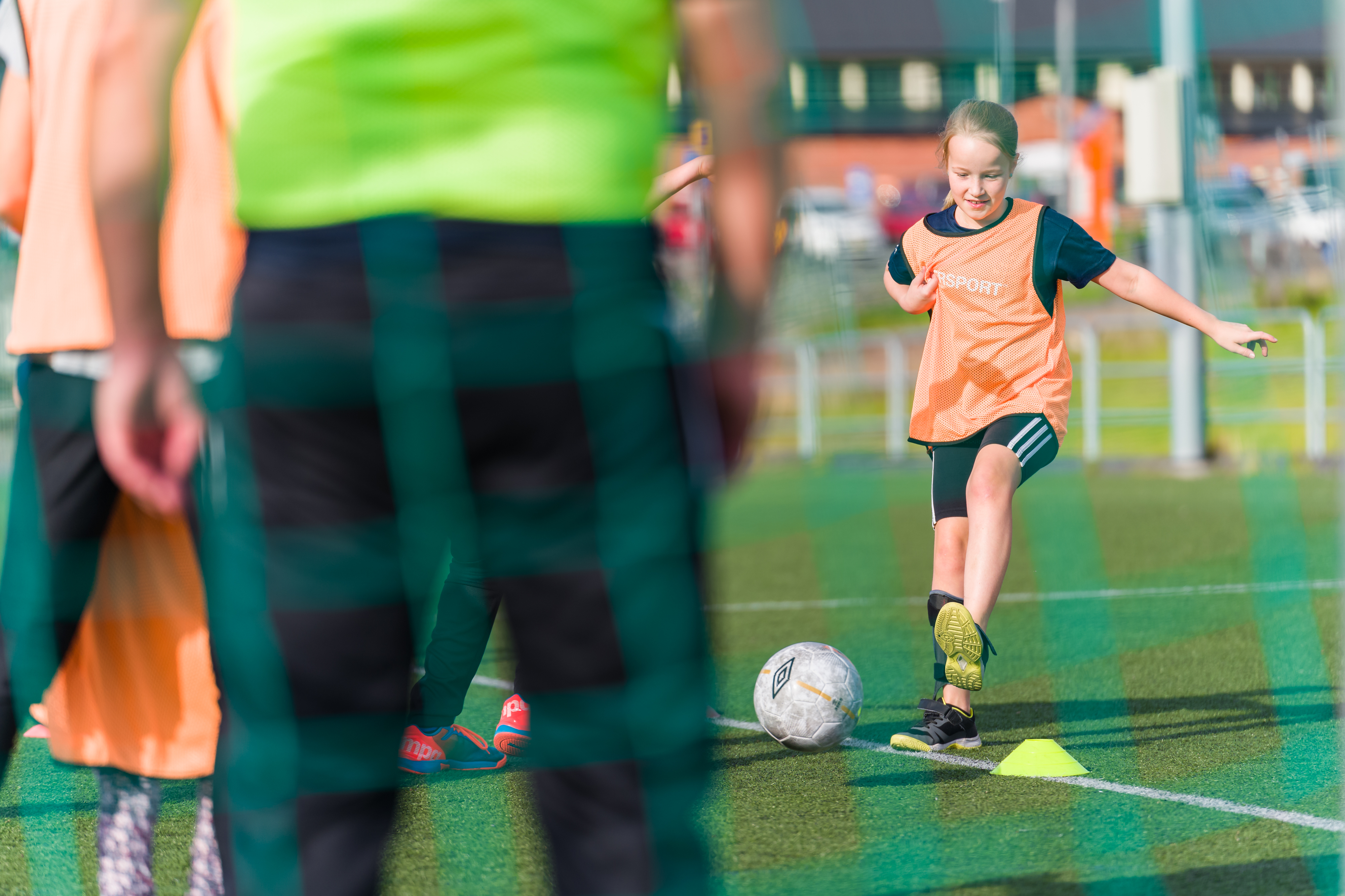 Flicka framför mål gör sig redo att skjuta. I förgrunden syns flera spelare och nätet i målet.