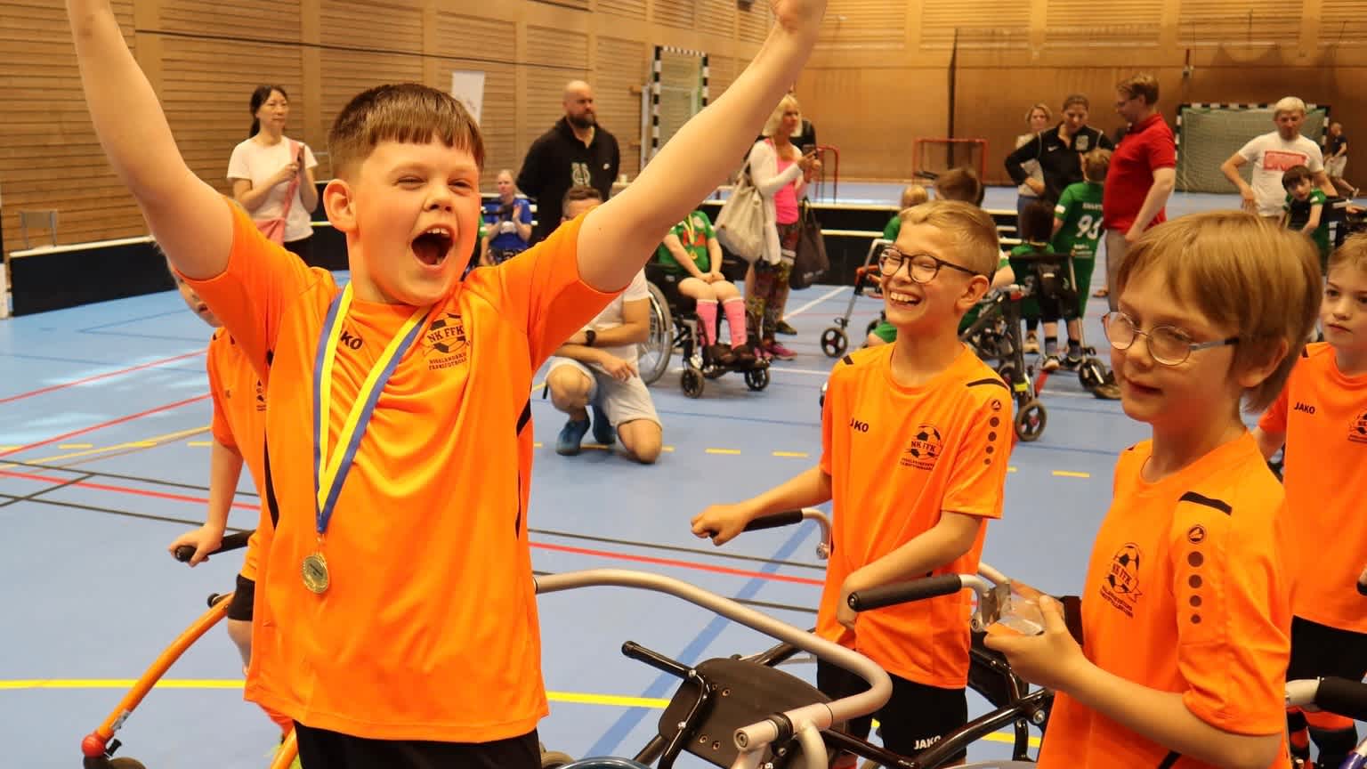 Inomhusmiljö, idrottshall. Tre glada framefotbollsspelare varav en med händerna uppsträckta i luften som en segergest och med en medalj runt halsen.