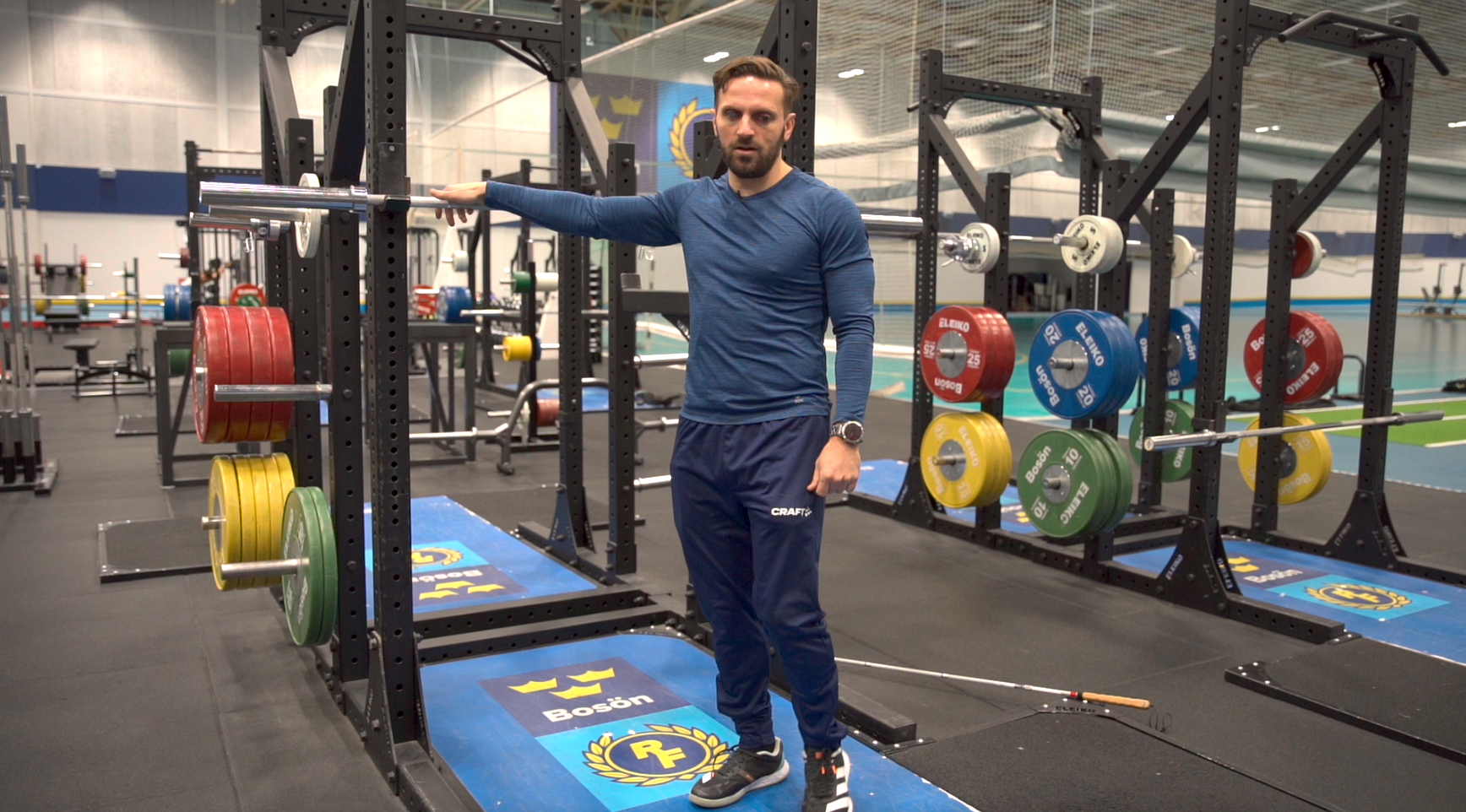 Inomhusmiljö, gym. En man står med handen på en skivstångsställning. I bakgrunden gymutrustning.