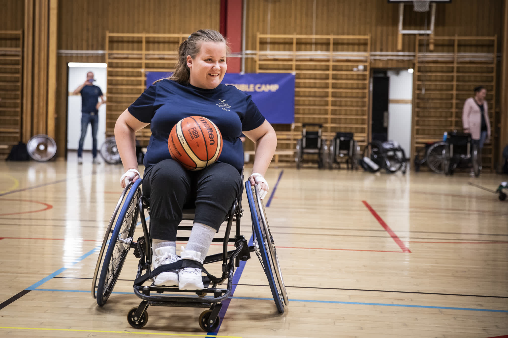 En tjej i rullstol på basketplanen med bollen i knät.