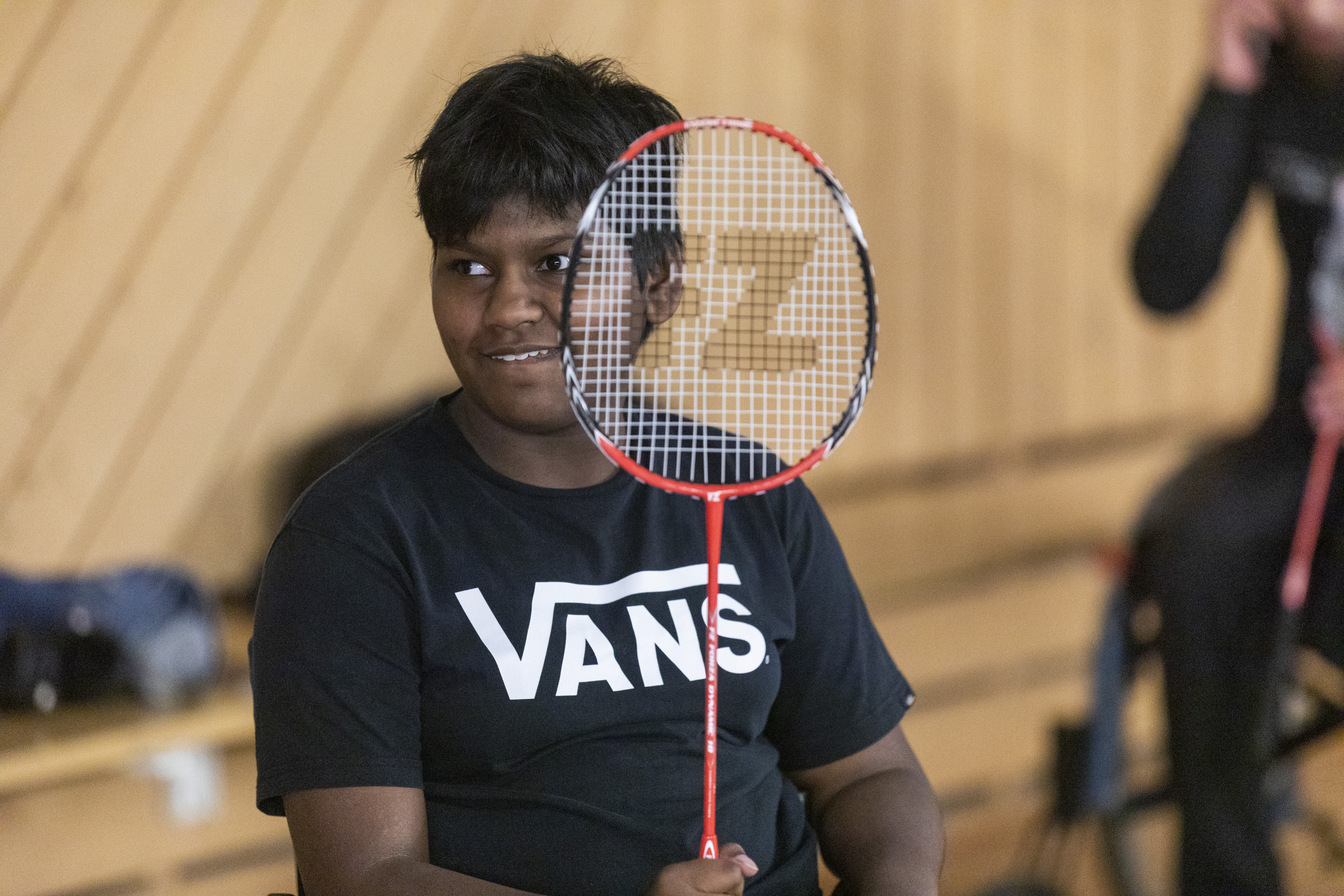 En kille sitter och håller upp ett badmintonracket.