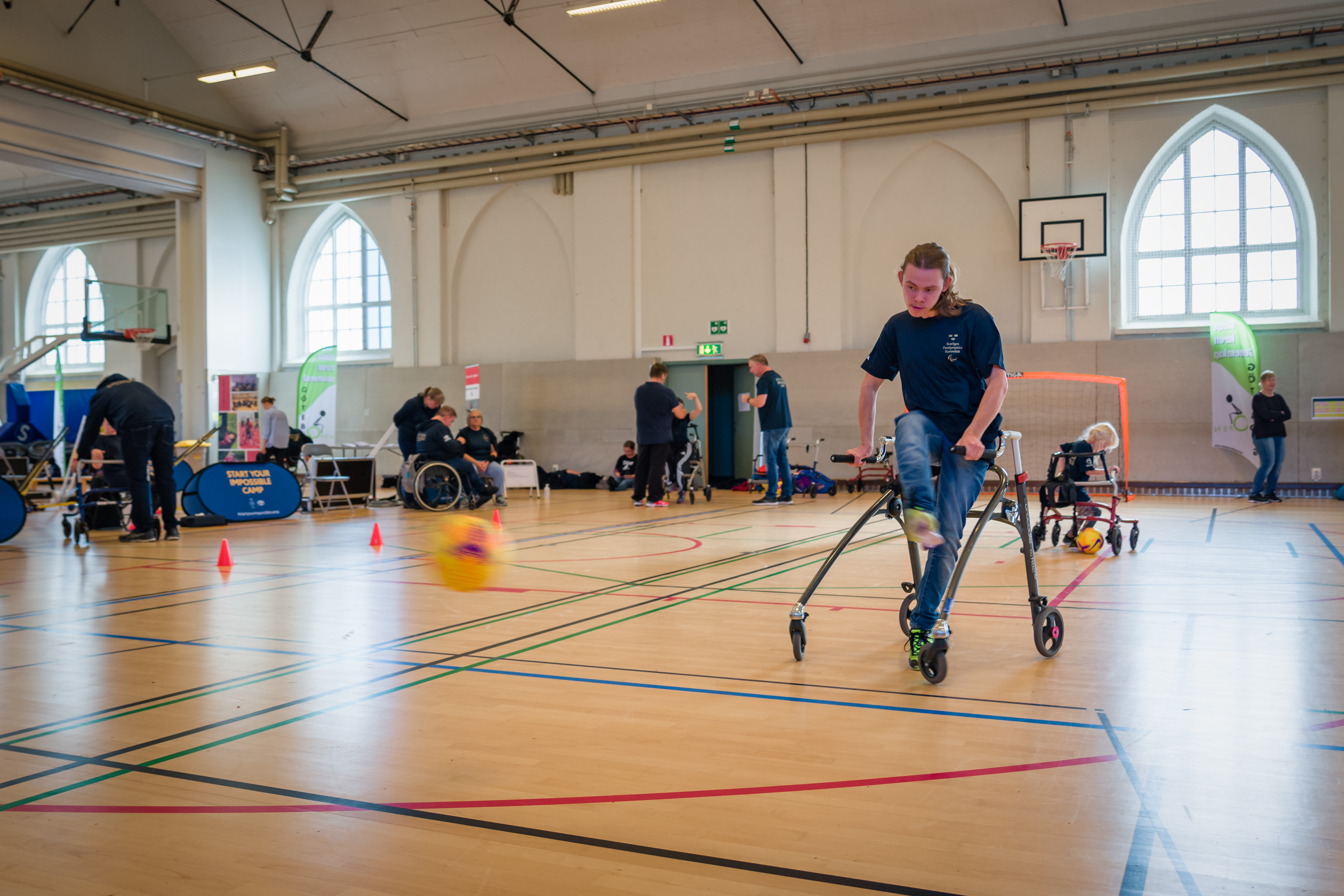 Ung kille har precis skjutit iväg ett skott. Bollen syns suddig i bild. I bakgrunden dribblar en liten tjej med en boll. 
