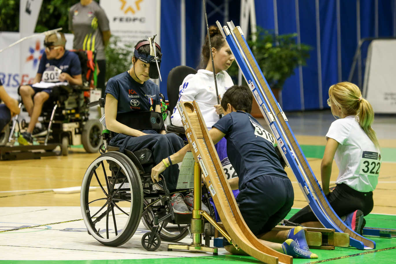 Maria med assistent under en match i boccia. Maria sitter i rullstol och spelar med en ränna. 