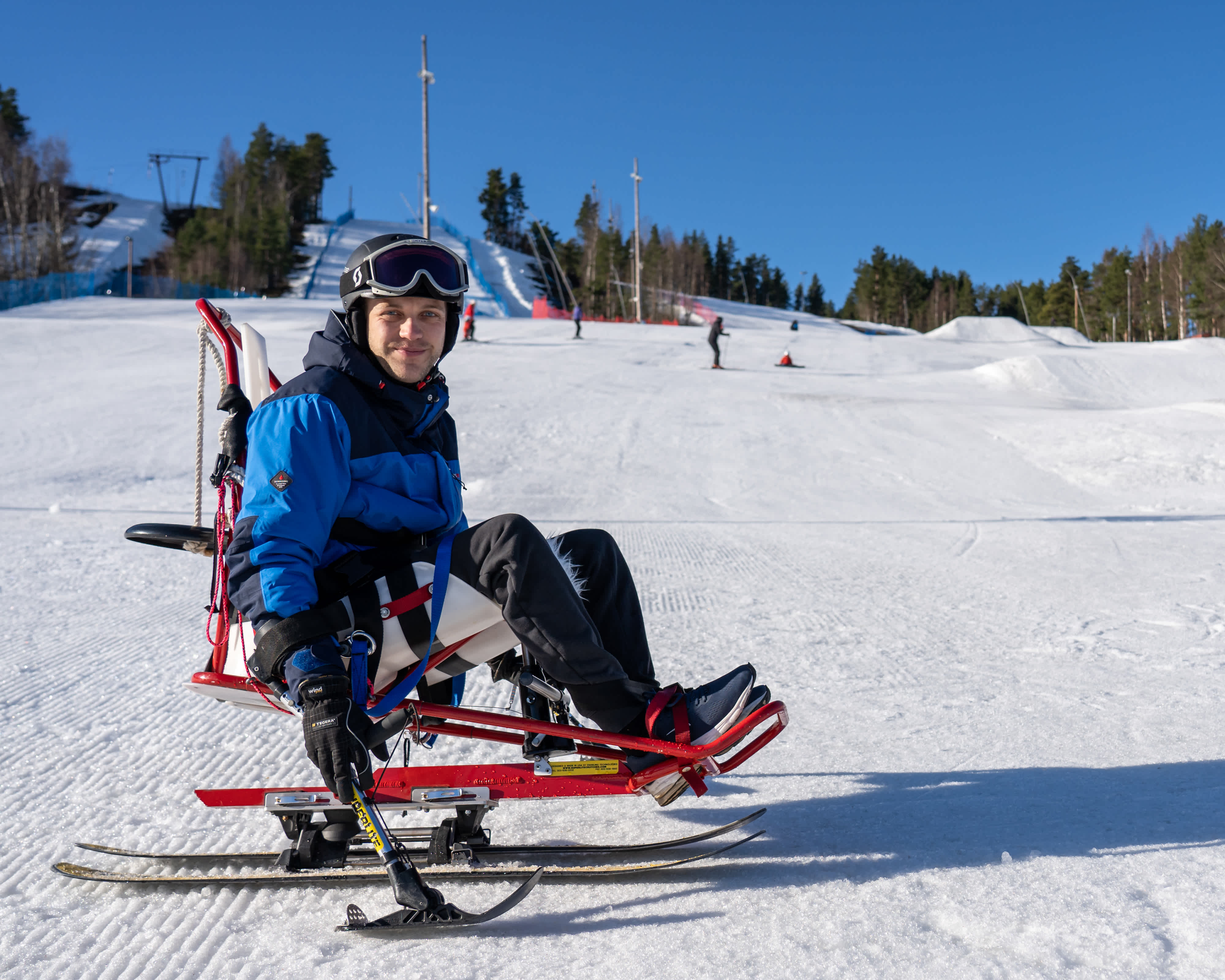 En skidåkare på sitski i slalombacken tittar in i kameran.