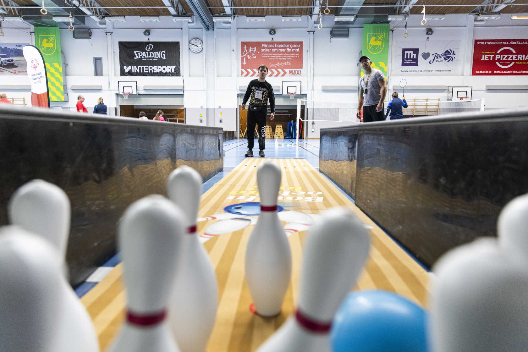 Ett bowlingklot slår ner käglor, på andra sidan banan står personen som släppt iväg klotet och tittar på.