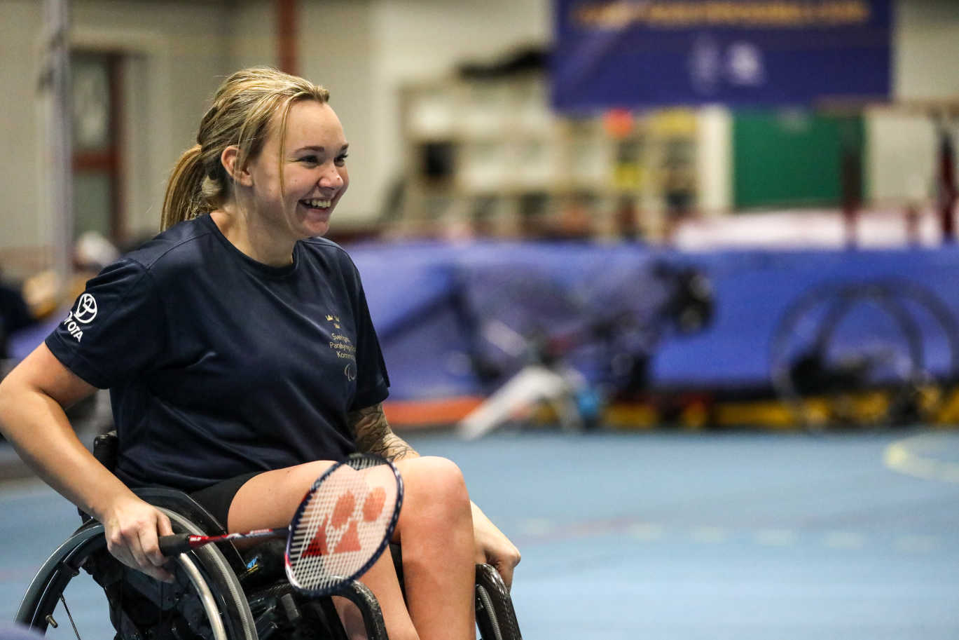 En tjej i rullstol skrattar när hon spelar badminton.