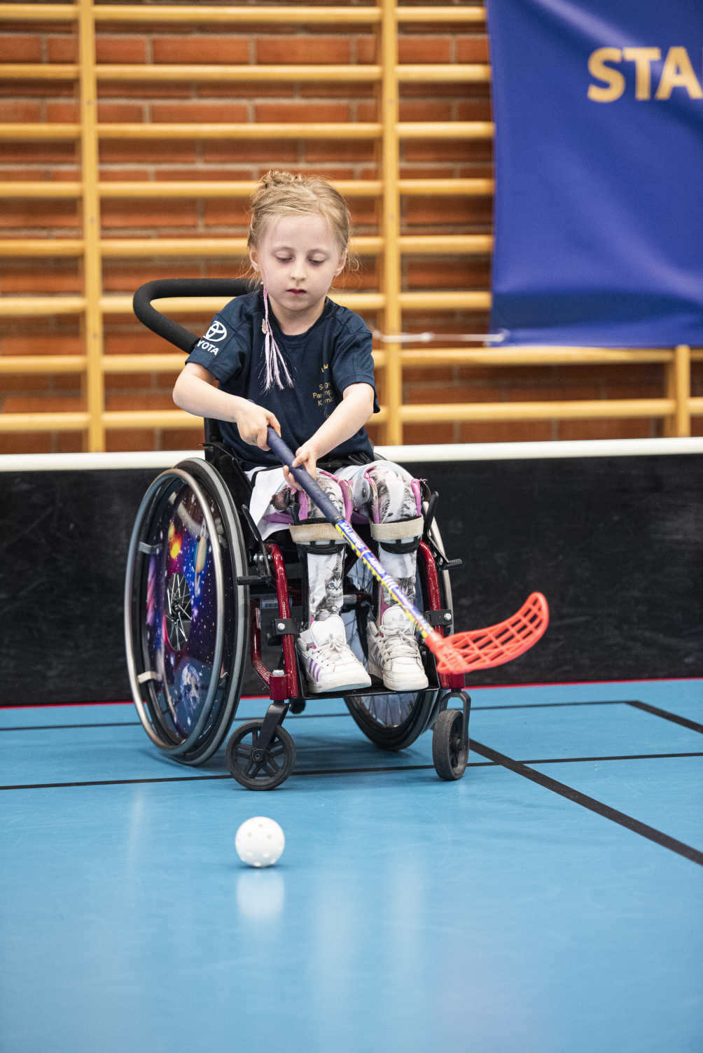 En flicka spelar rullstolsinnebandy i en idrottshall.