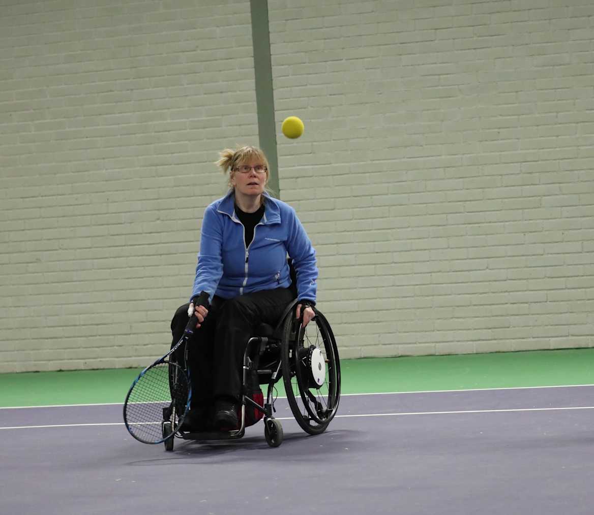 Kvinna på väg att slå till tennisbollen som flyger mot henne.