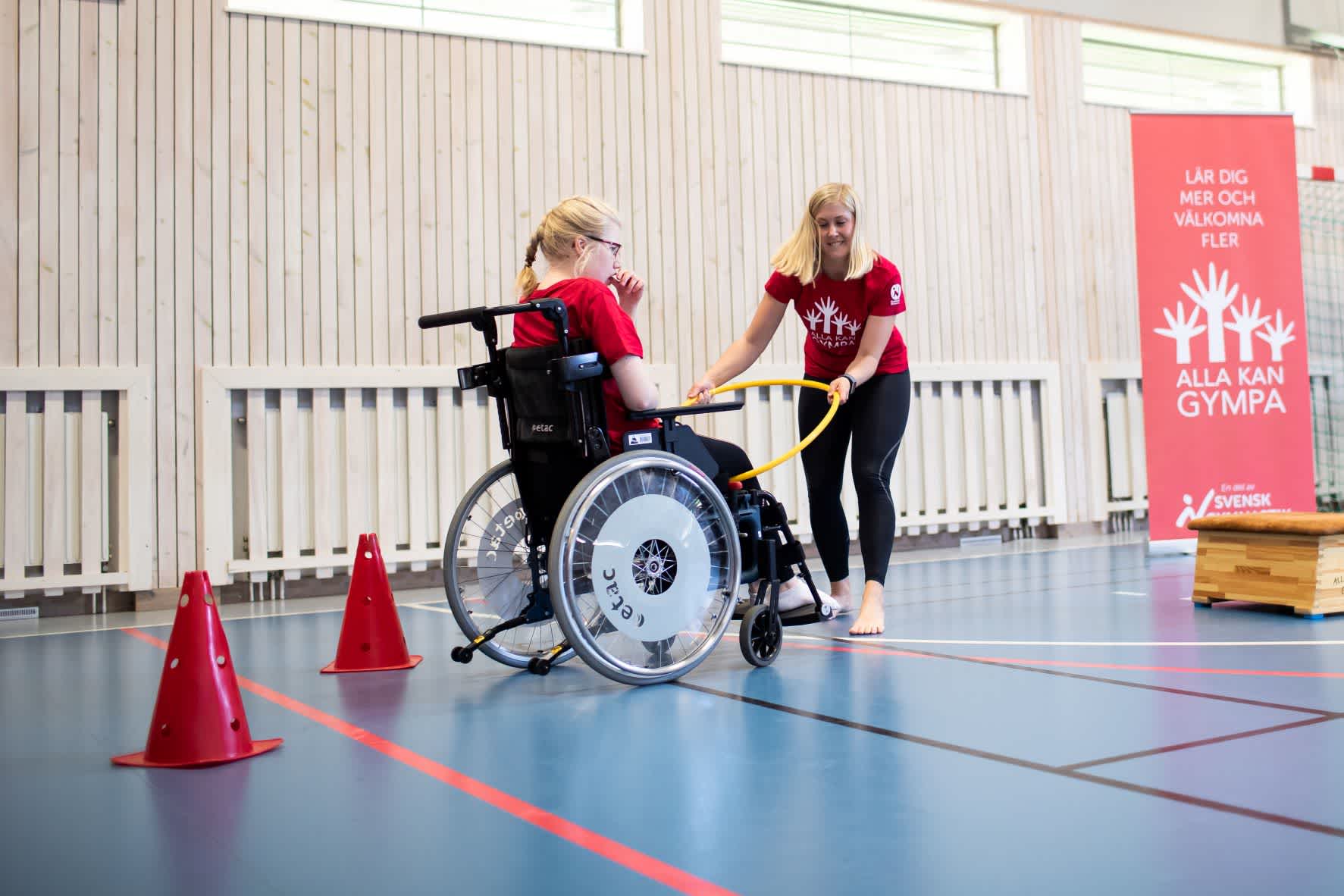 En flicka i rullstol utför en övning tillsammans med en ledare.