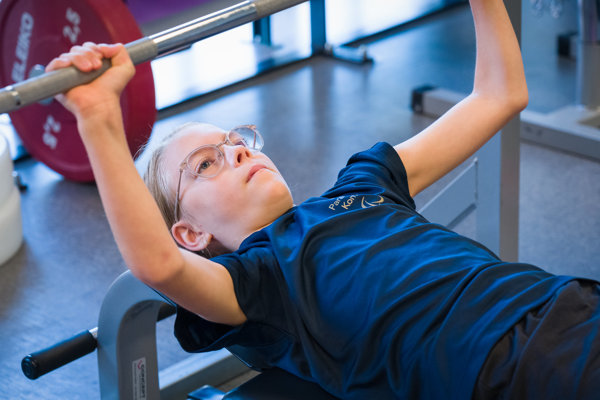 Ung tjej med blicken fokuserad på stången, skjuter den ifrån sig, uppåt.