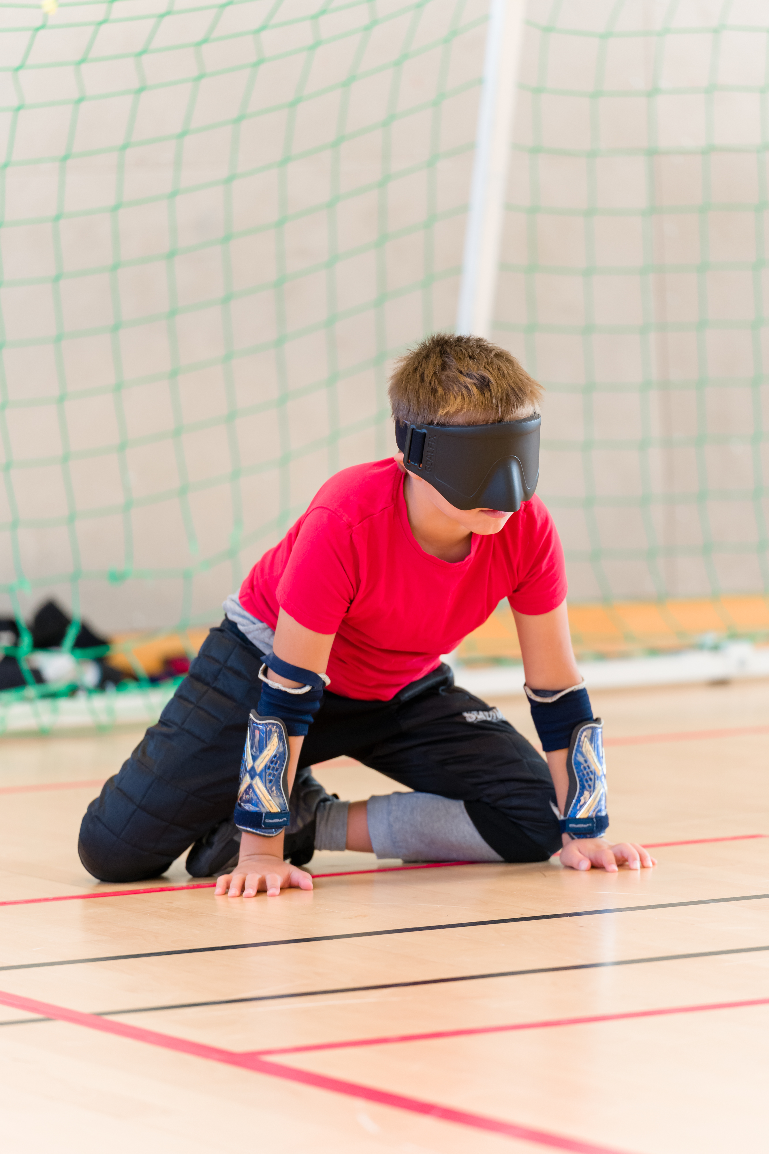 Kille är redo att försvara sitt mål, han sitter på knä framför målet med händerna i golvet.