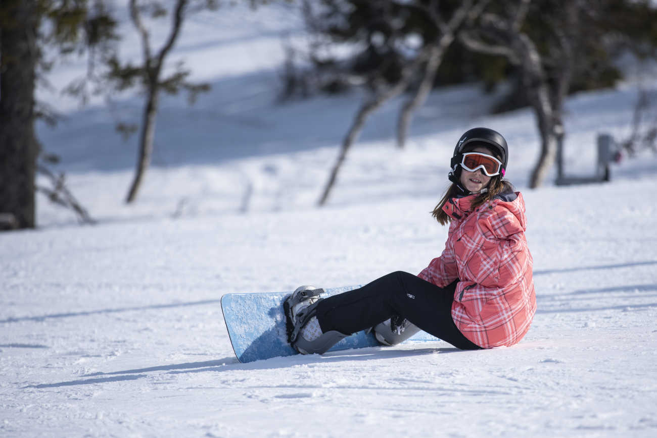 En tjej med snowboard på fötterna sitter ner i backen. 