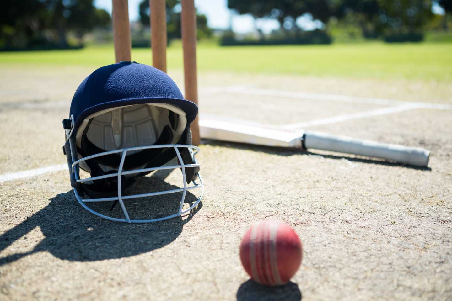 På en cricket bana ligger en crickethjälm, boll och cricketträ.