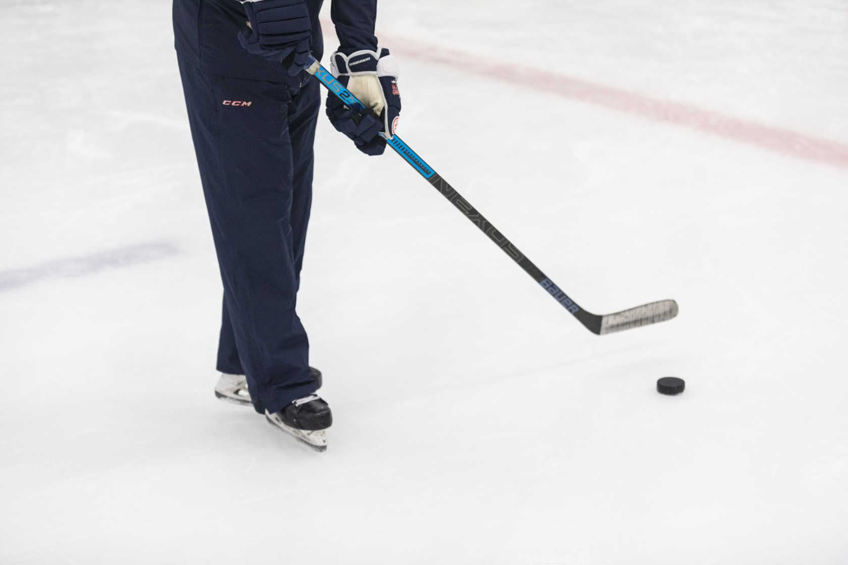 En person står på isen med ishockeyklubba och puck. Man ser endast benen på personen.