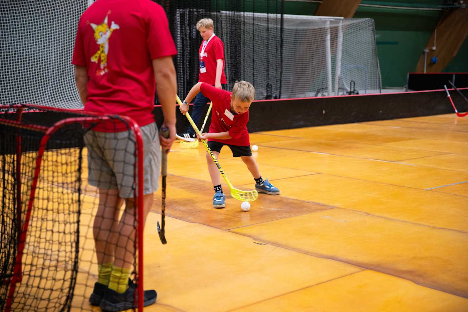 Foto, inomhus. En pojke dribblar med en innebandyboll framför ett mål.