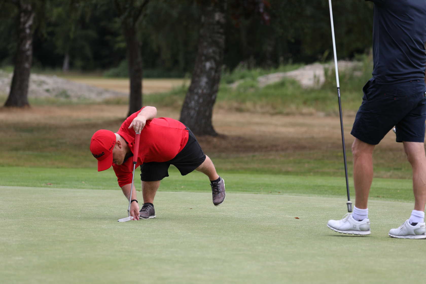 Man med kortvuxenhet böjer sig ned för att ta upp golfbollen hur hålet.