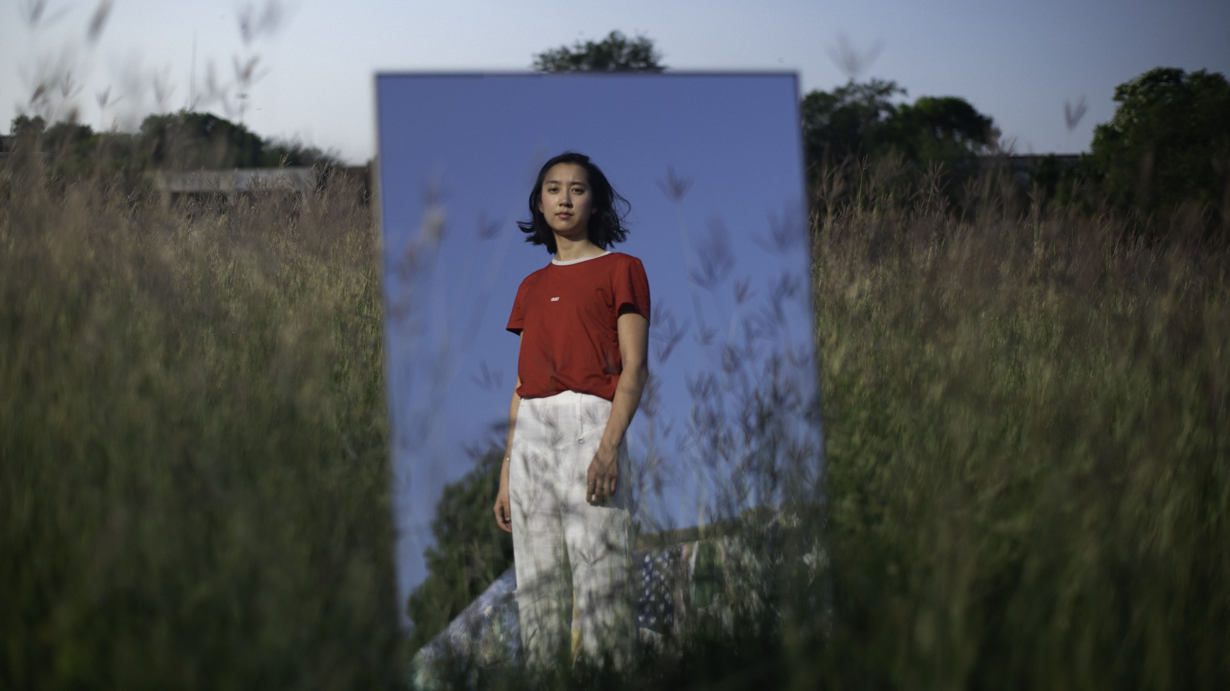 Portrait of a woman with shoulder length hair looking at her reflection in a mirror, wearing a t-shirt