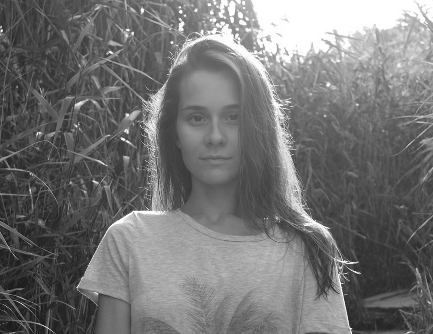 Olha Zhurba looking directly at the camera. She is standing in a field and is surrounded by tall crops. Black and white portrait. 