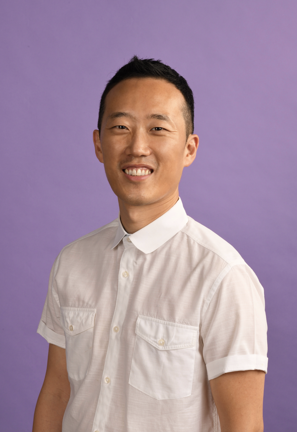 Producer Eddie Kim wears a white shirt against a purple background.