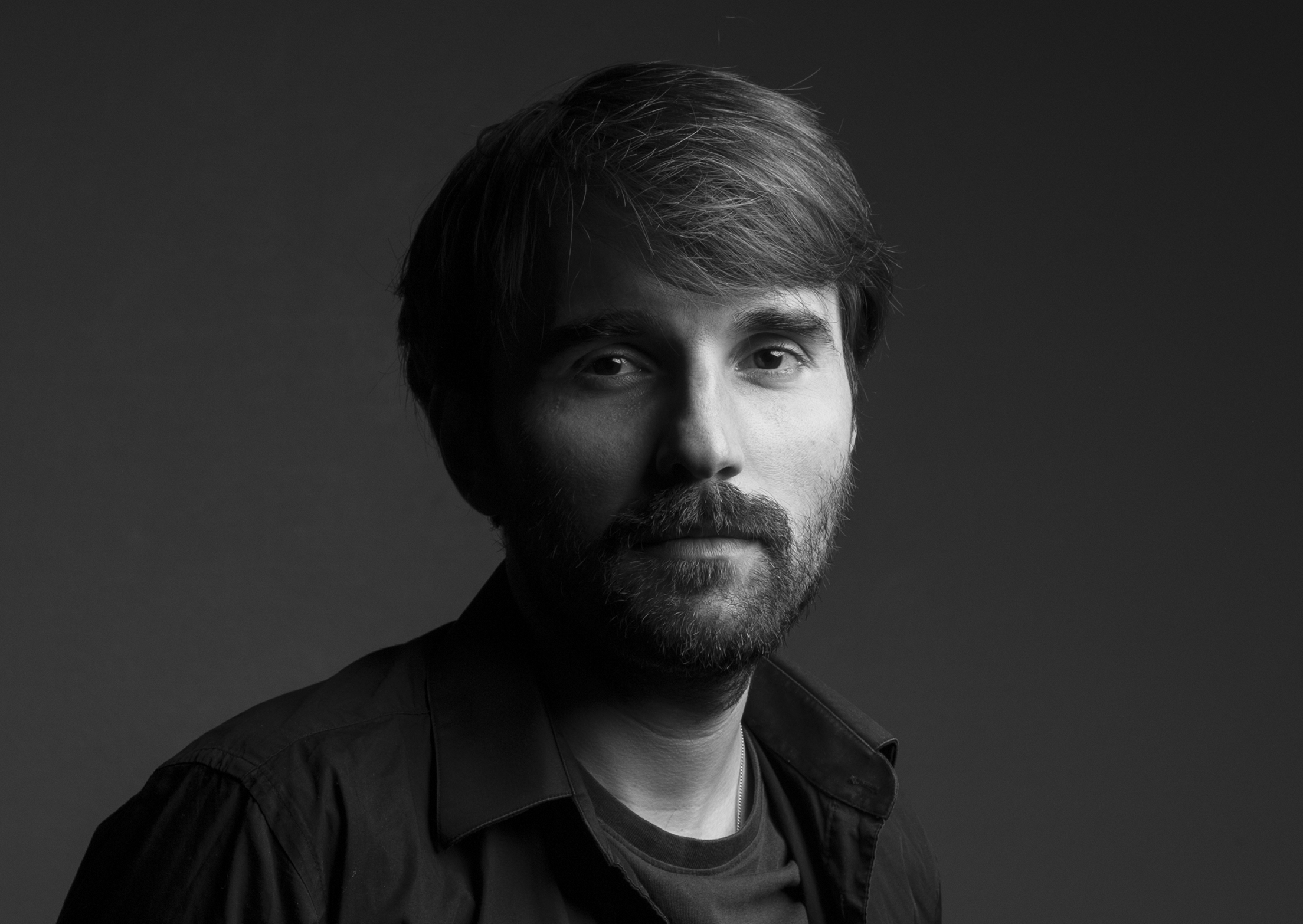 Headshot of a man with short hair, beard, wearing a shirt with a t-shirt underneath. 