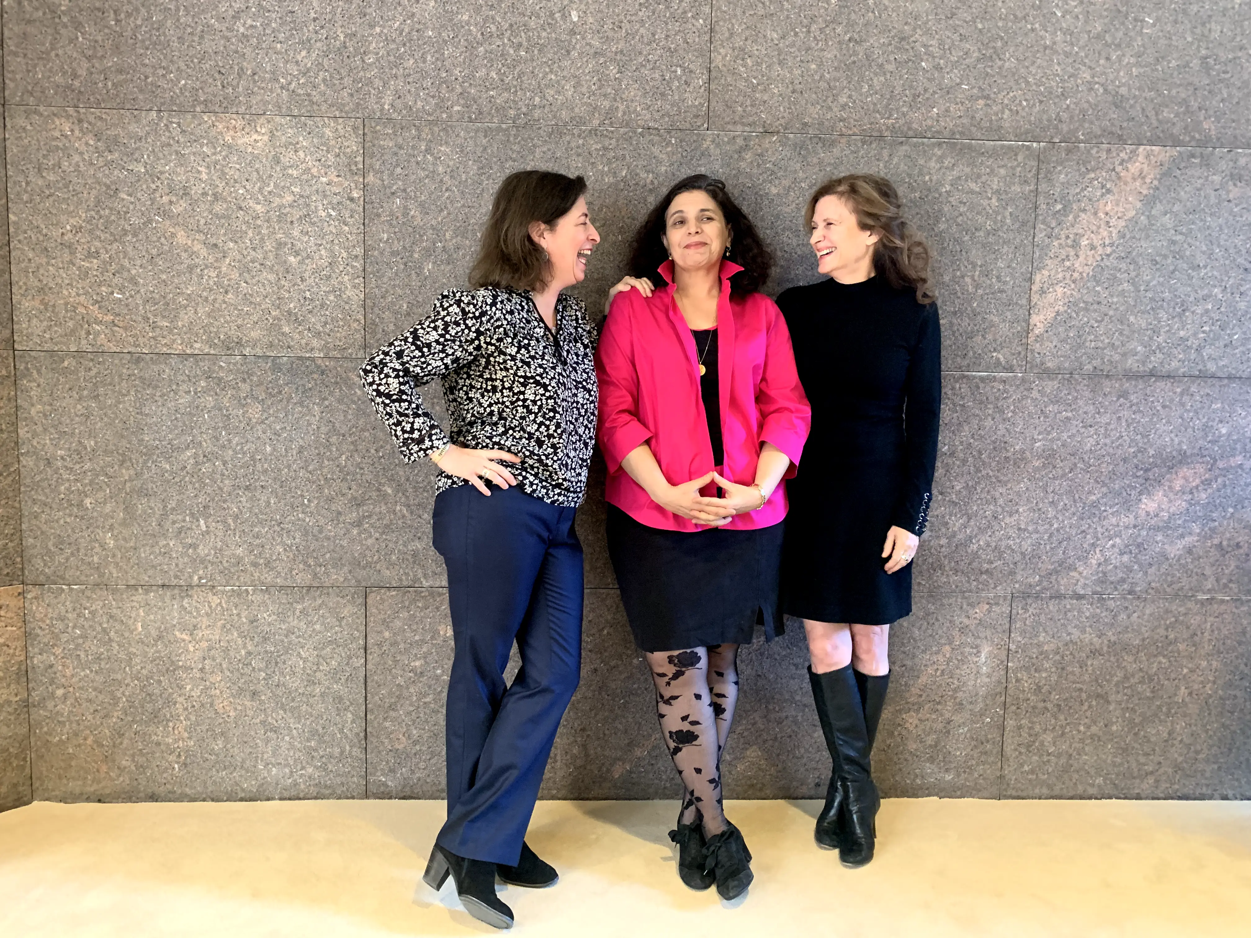 Co-founders from left to right Julie Parker Benello, Judith Helfand, and Wendy Ettinger. The three women are standing together up against a gray stone wall. 