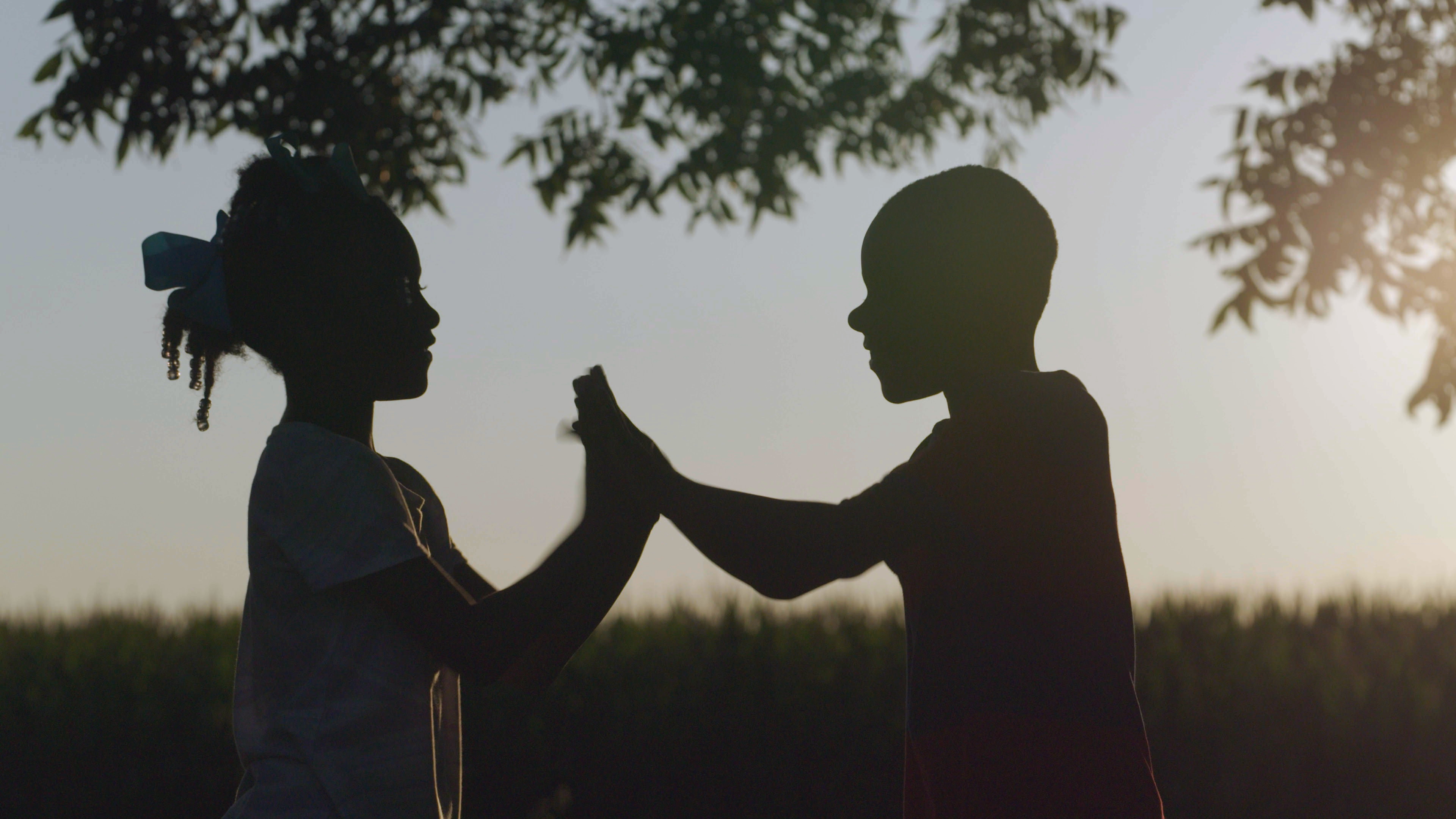 Two children play patty cake in a field.