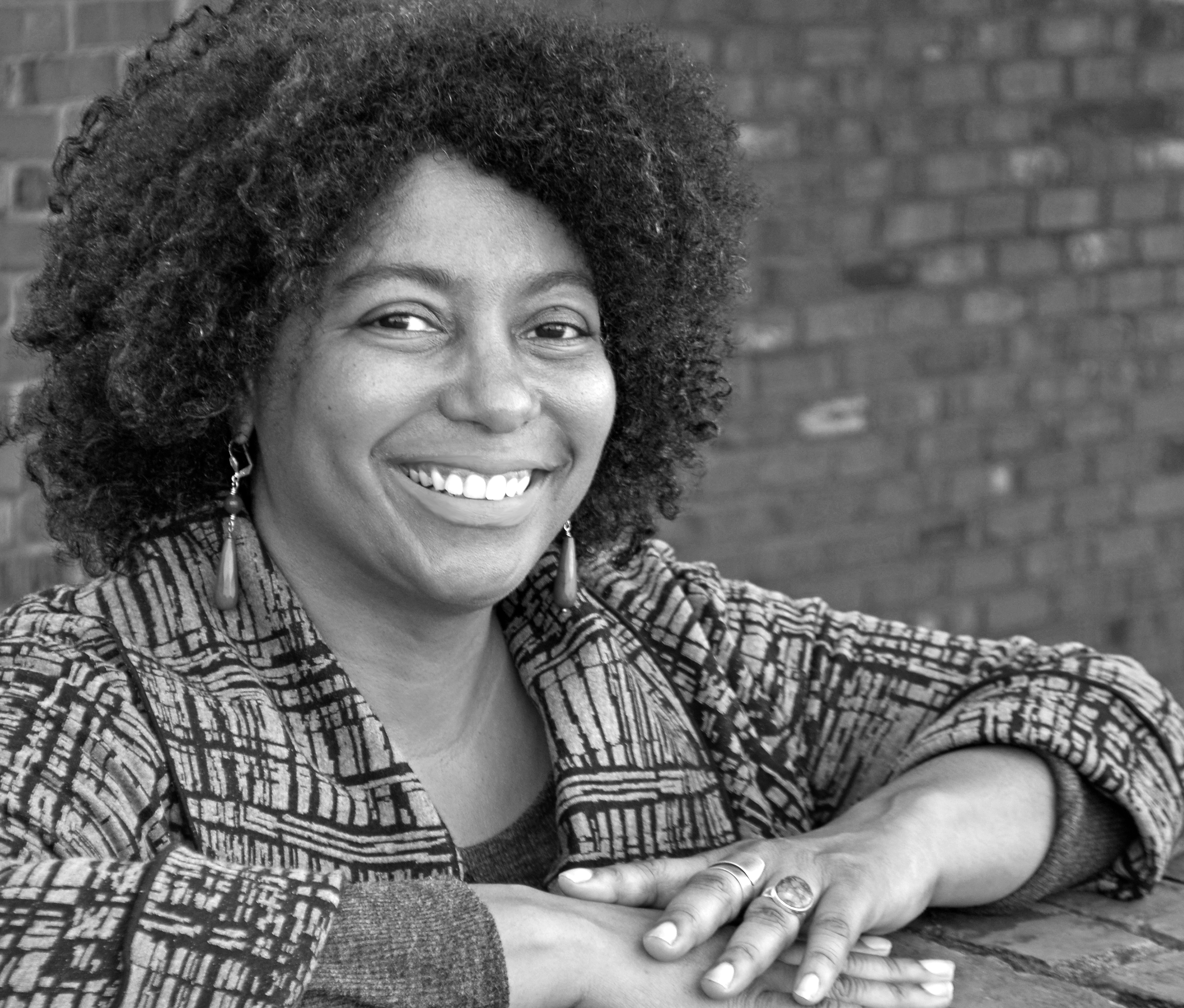 Jacqueline Olive is smiling and looking directly at the camera. She has shoulder-length hair. Portrait in black and white.