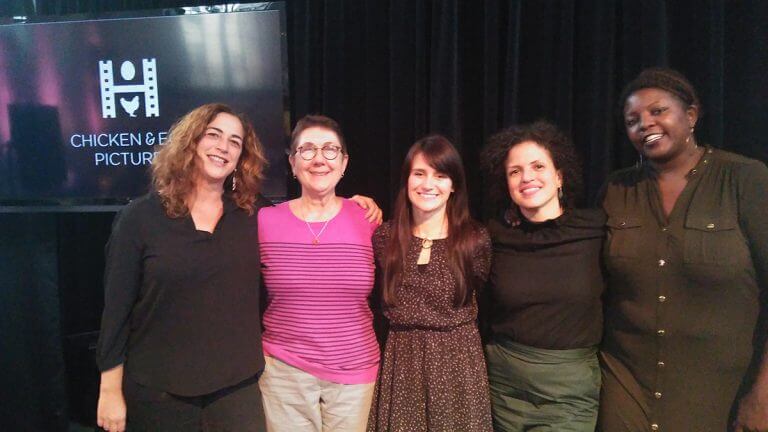 Kristine Jacobson, Julia Reichert, Elaine McMillion Sheldon, Michele Stephenson, and Yoruba Richen look at the camera and smile. In the background is a screen with the Chicken & Egg Pictures logo.