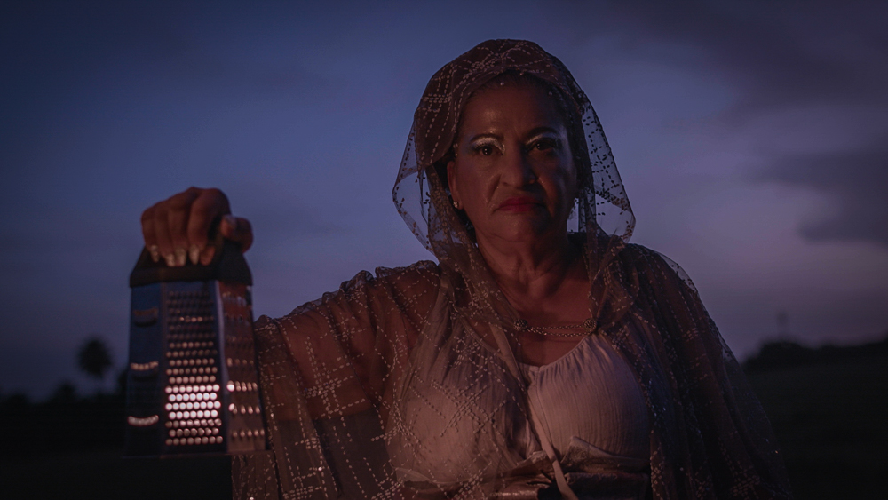 Still from Matinino. Idaliz with a silver cape holds a lantern as she walks through the night sky.