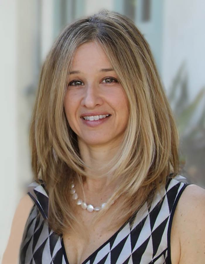 Portrait of Jessica Levin, she has a v neck blouse, a necklace, medium length hair parted in the middle