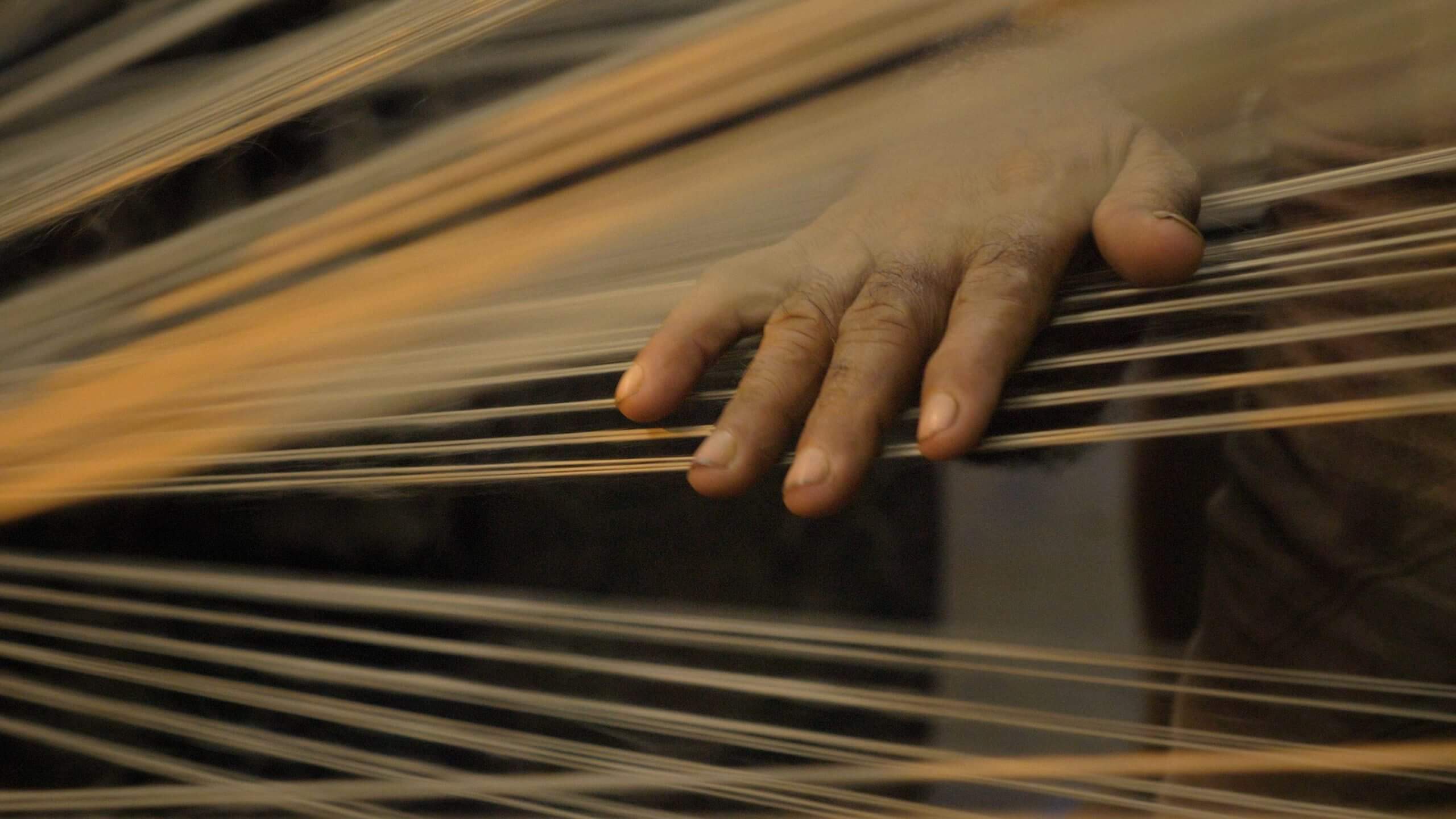 Still from The Golden Thread.  A workers hand on jute threads as they pass through the spinning machine