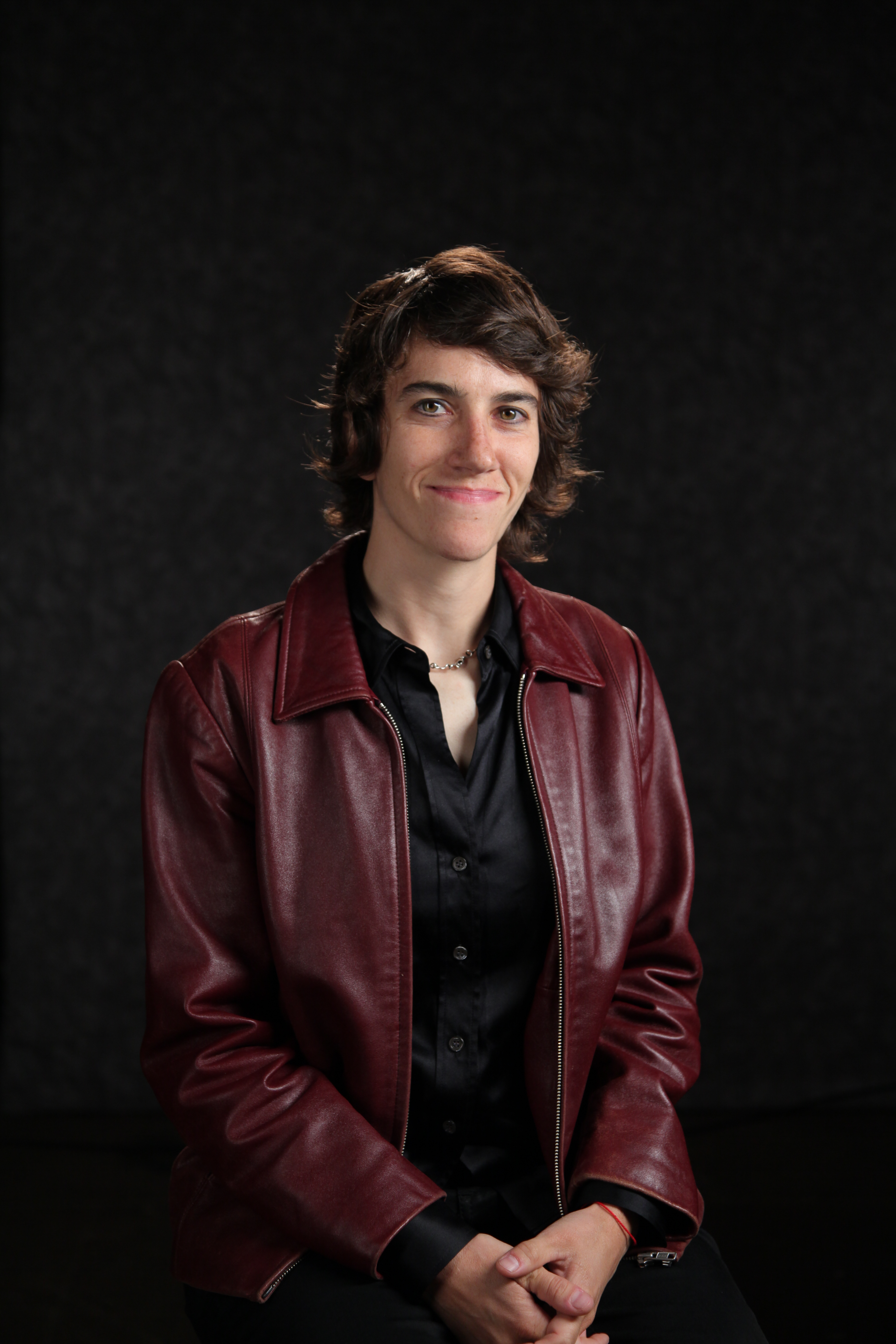 Headshot of Sally Rubin. Sally smiles slightly at the camera and wears a buttoned shirt, a leather jacket, and a necklace. Sally's hair is short and parted to the right.