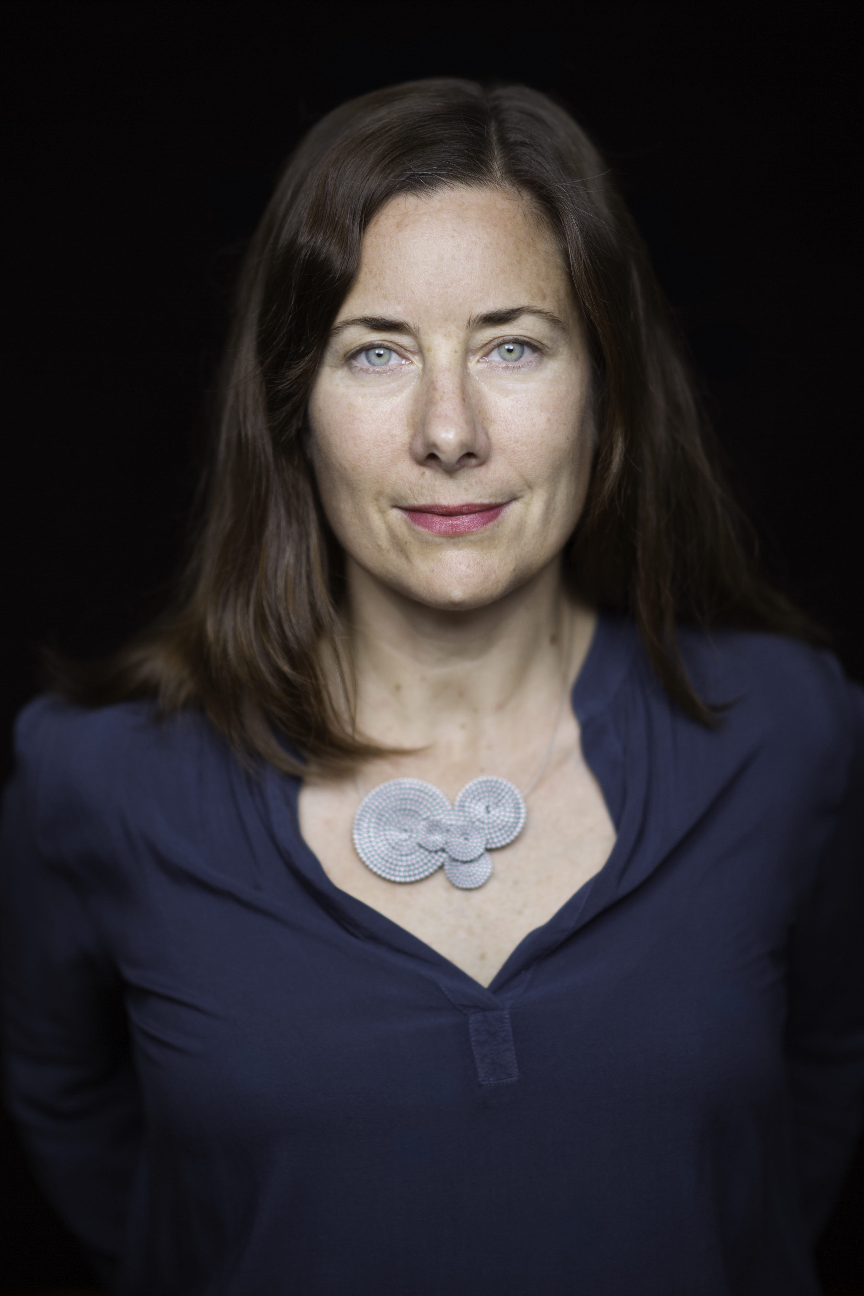 Jennifer Redfearn looking directly at the camera. She wears a necklace and a blouse. Her hair is medium length and parted in the middle. 