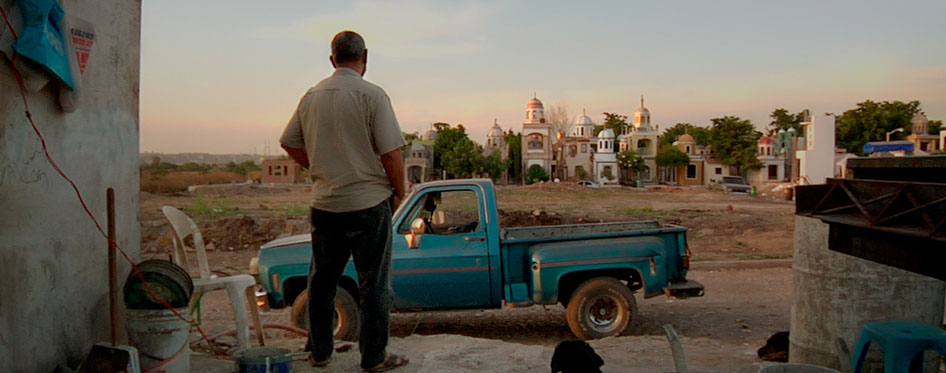 man looks at blue truck amongst a landscape of a town. 