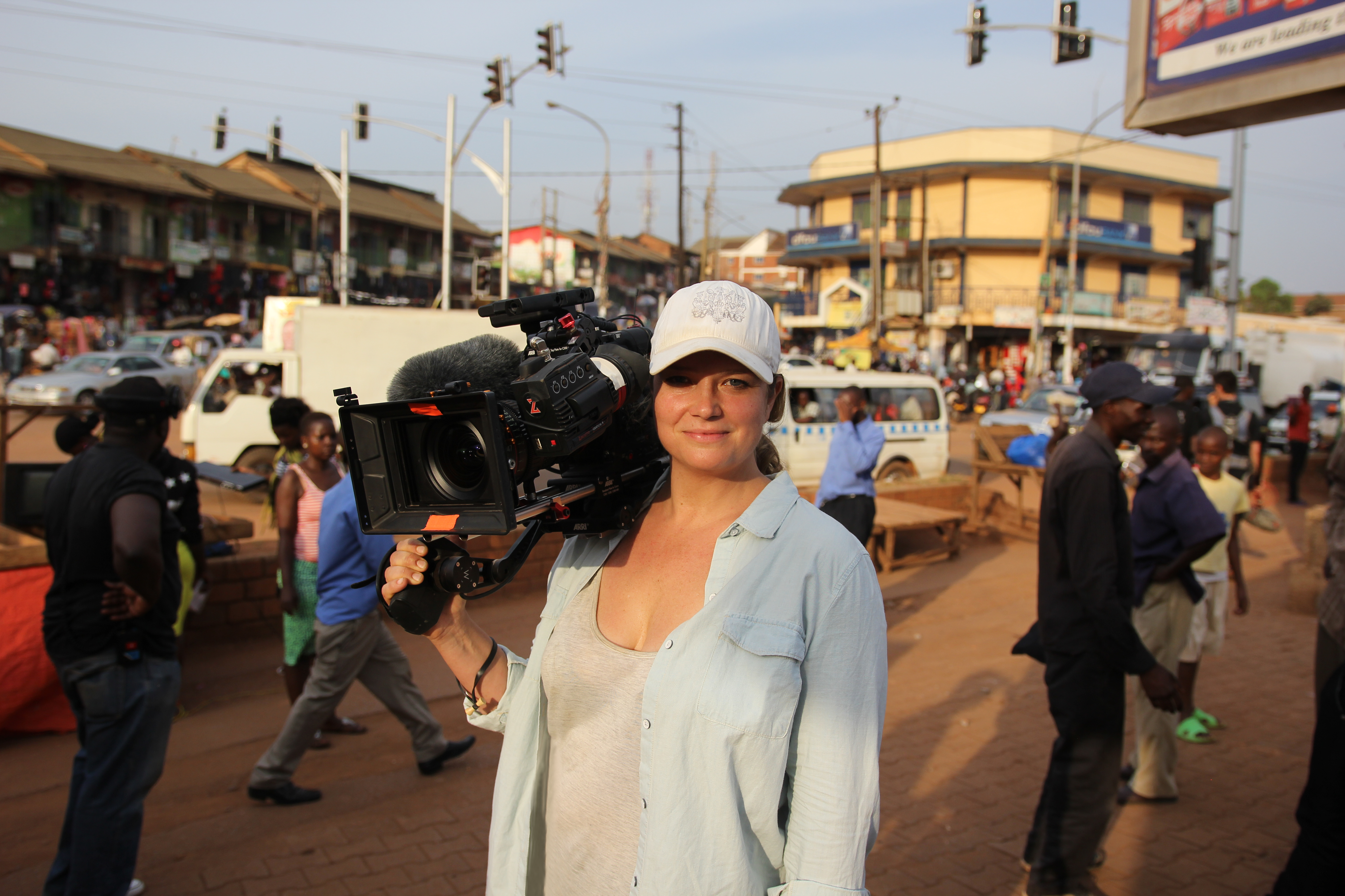 Cathryne Czubek holds a big camera on the streets of Uganda and smiles.