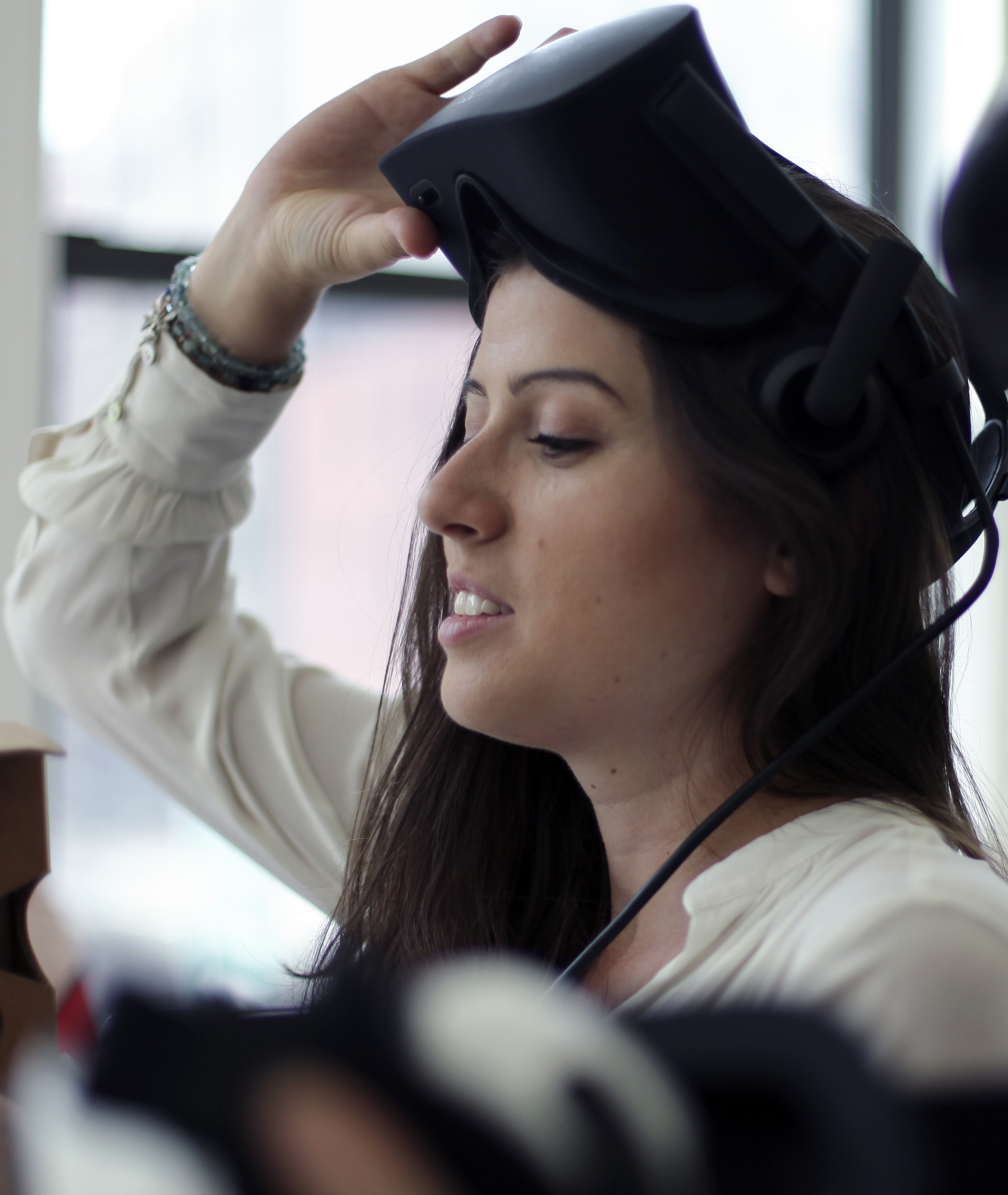 A photo of a woman lifting a VR headshot off of her eyes.