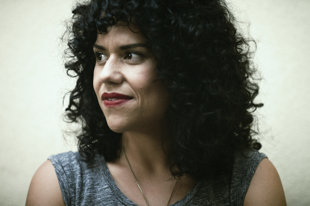 Cecilia Aldarondo is looking away from the camera. She has medium curly hair and is wearing lipstick. 