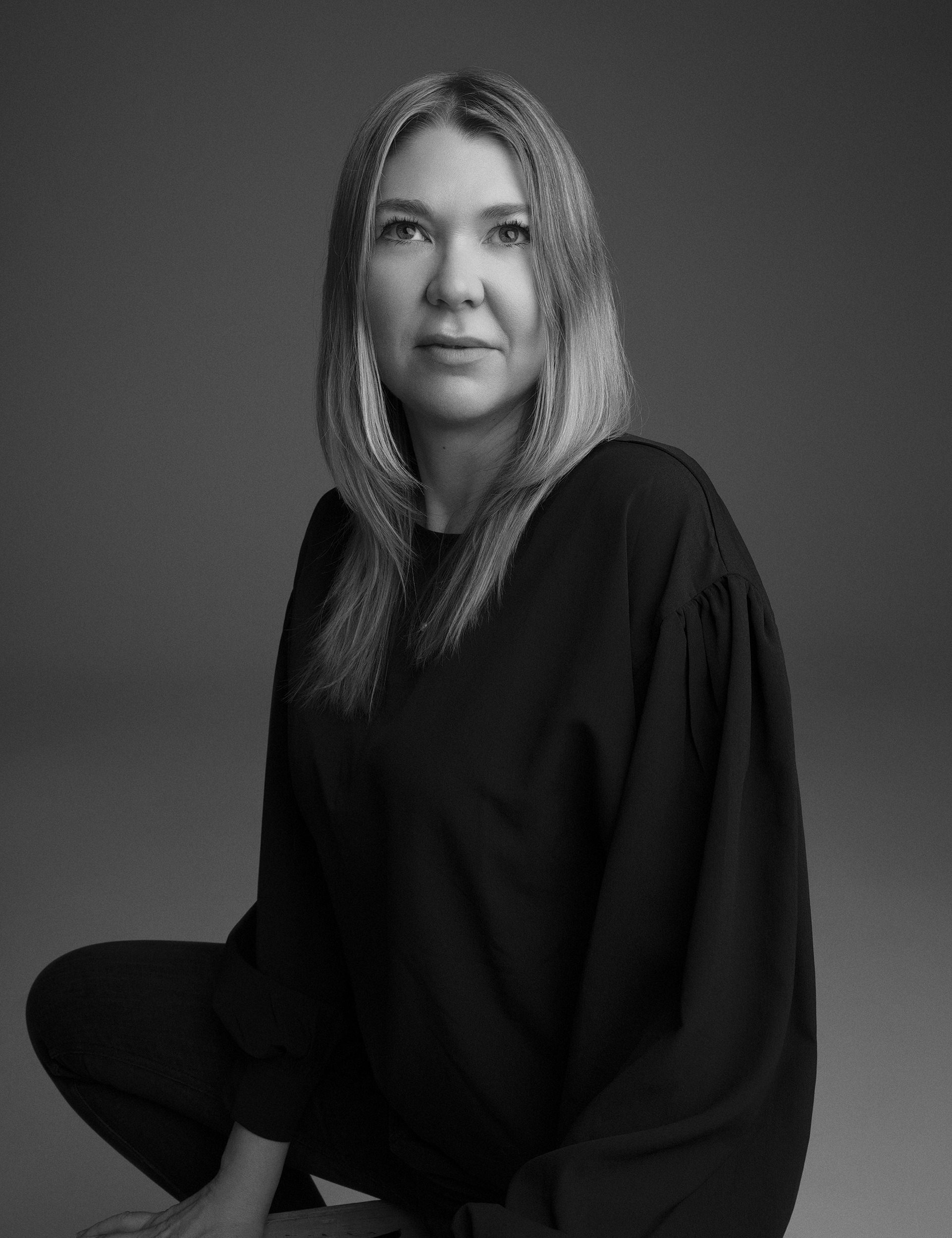 Mia Donovan looks away from the camera. She wears a dark outfit. Portrait in black and white.