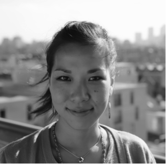 A black and white portrait of a woman on the roof of a building smiling at the camera.