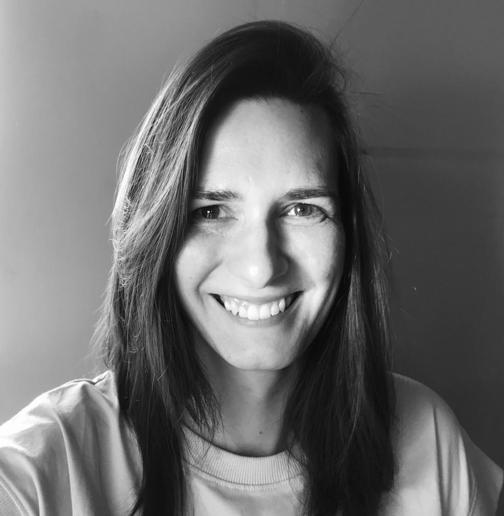 Kasia Kuczyńska looking directly at camera and is smiling. She has long, dark hair and is wearing a crew neck shirt. Black and white portrait. 