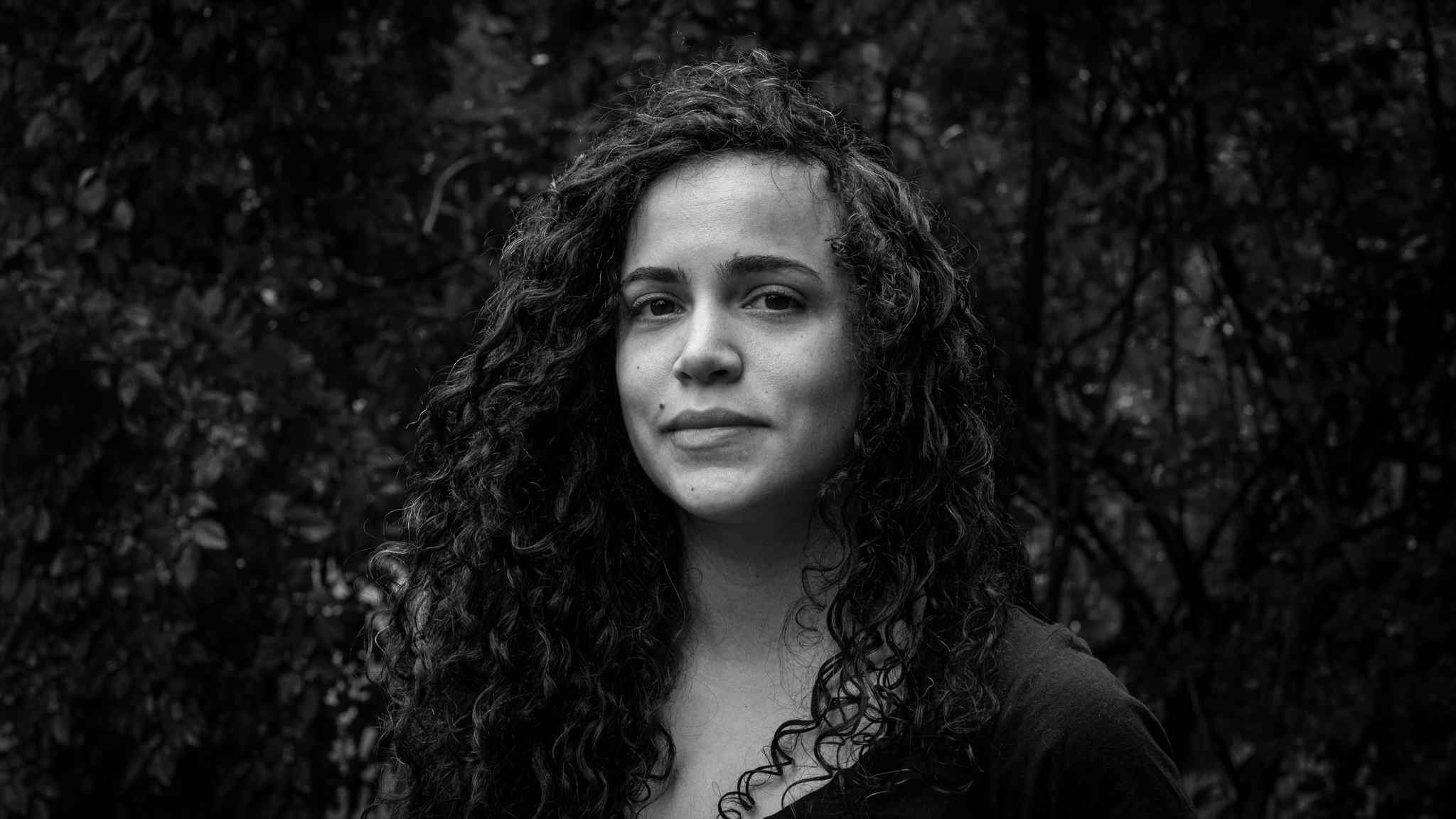 One of the producers for Matininó, Wendy Muñiz, a woman with curly long hair and a dark-colored shirt, poses for a black and white photo.