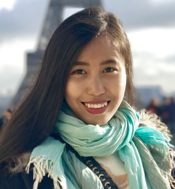 Snow (Hnin Ei Hlaing) is smiling at the camera, the Eiffel Tower is behind her.