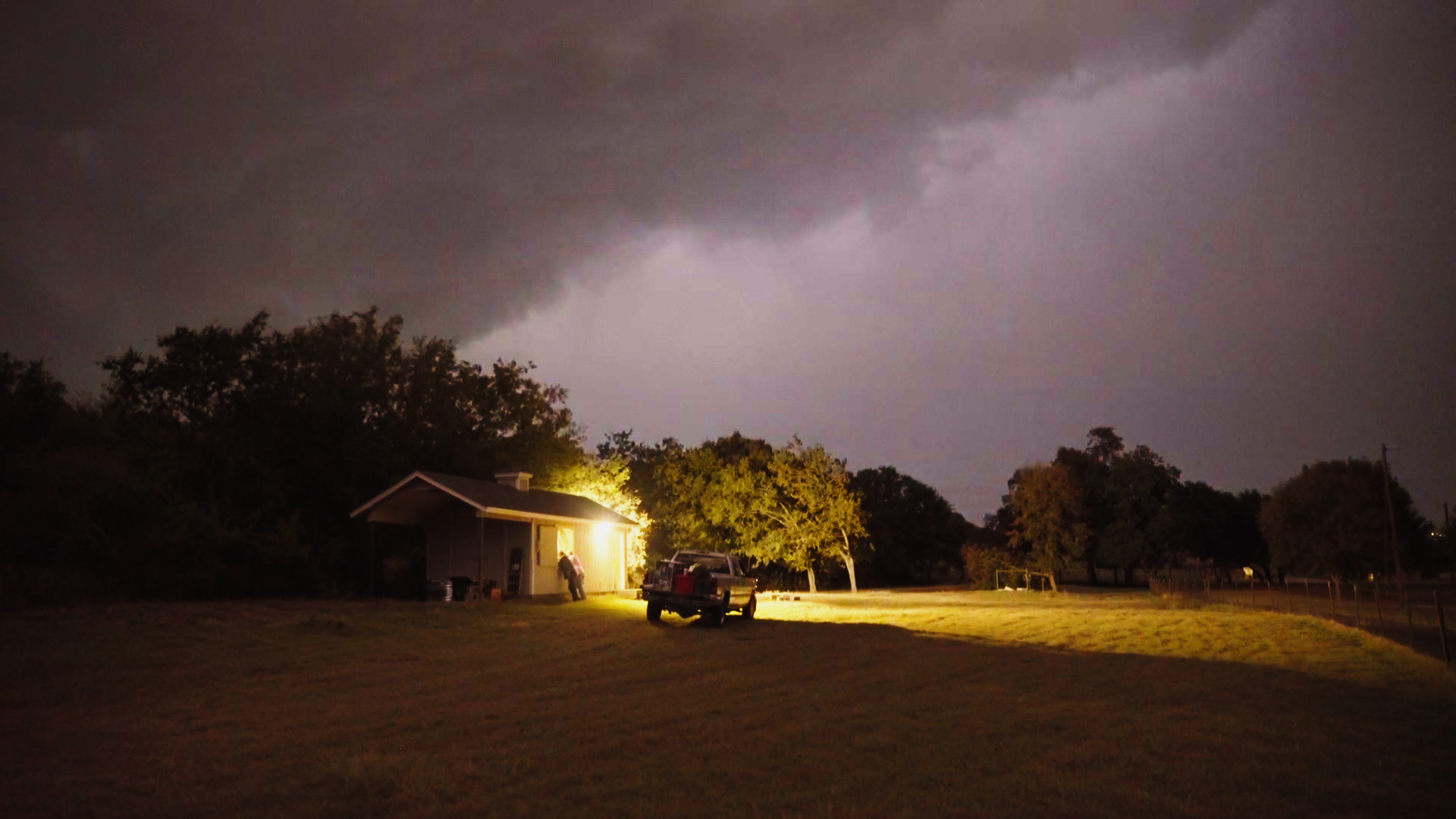 Light glows from a window of a small house in an open field.