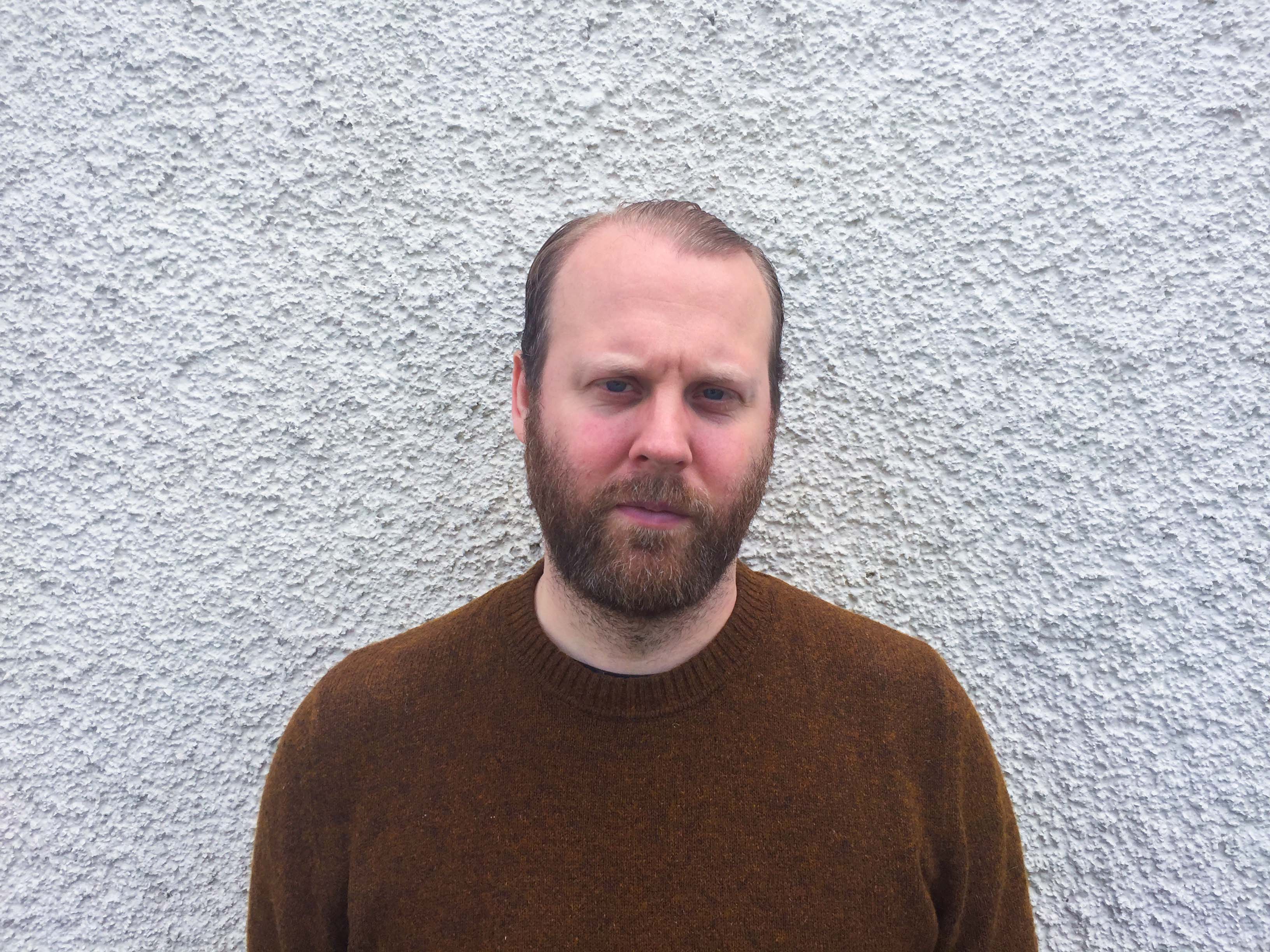 A portrait of Kristofer Henell in front of a white wall.