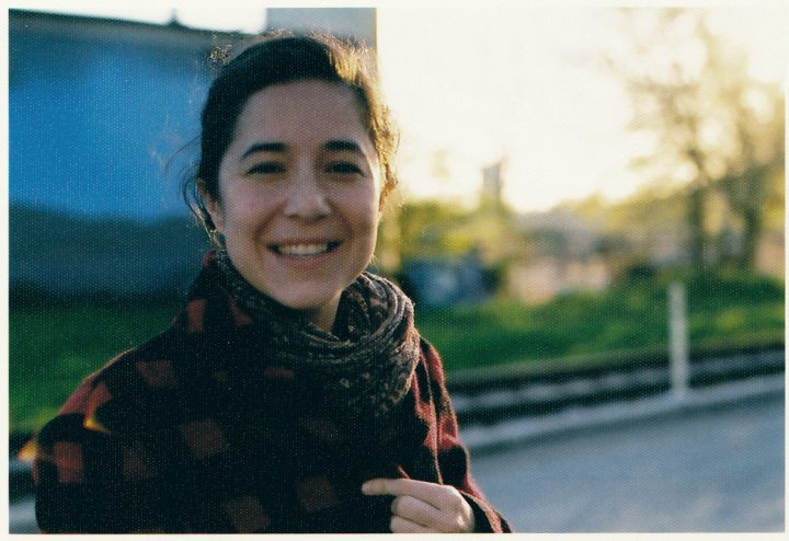 Ashley Sabin looking straight ahead and smiling. She is wearing a patterned shirt and scarf. Portrait with out of focus background.