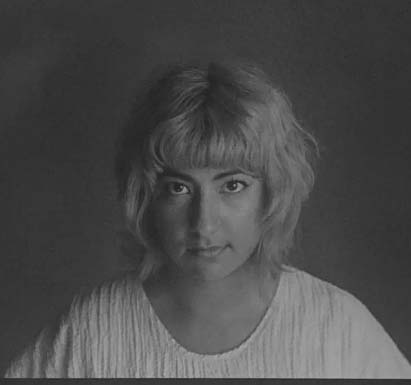 Portrait of a woman with short medium hair, slightly tilting down their head and looking up at the camera