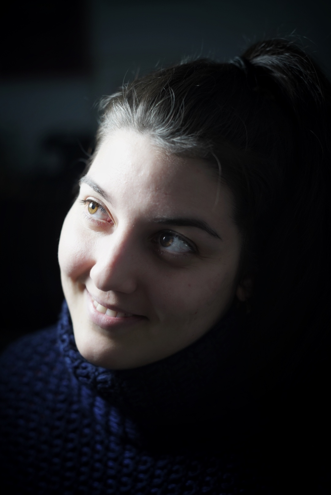 Color, chiaroscuro photograph of smiling young woman with big eyes. 