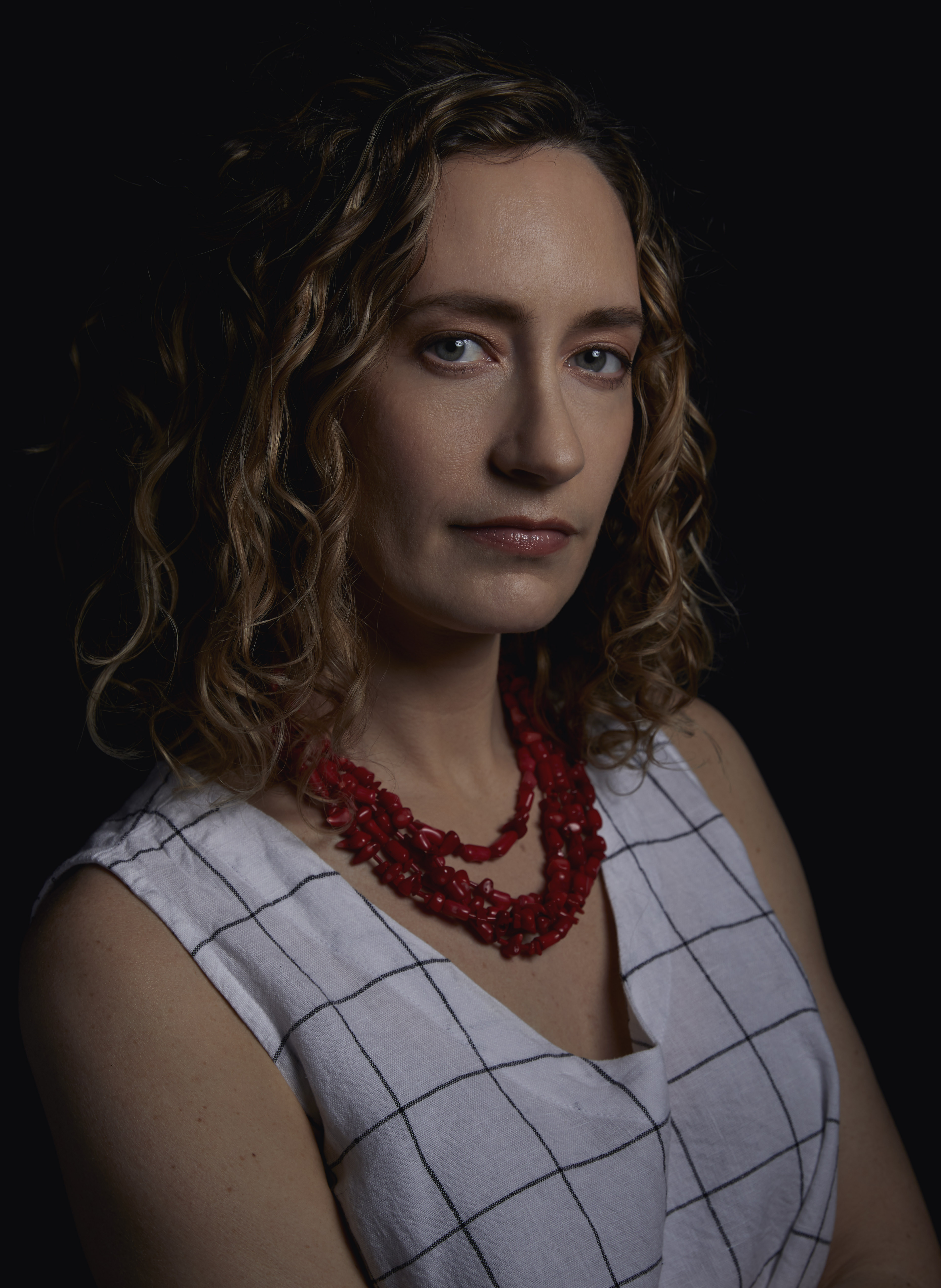 Black and white headshot of Sharon Shattuck from the shoulders up wearing a beaded necklace and white grid-striped tank