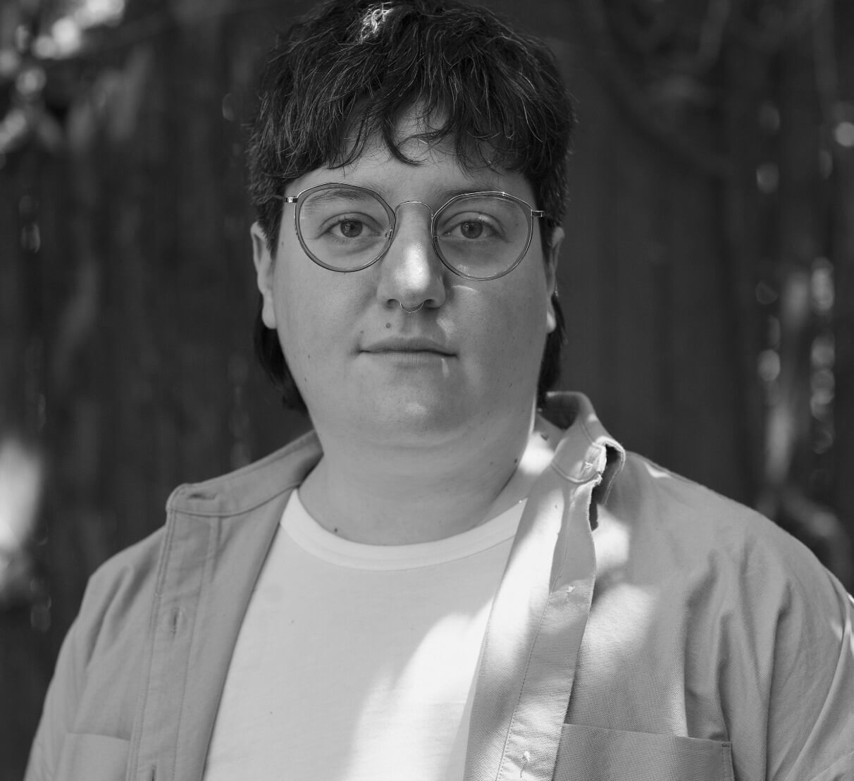 A white nonbinary person with short dark hair and glasses looks at the camera.